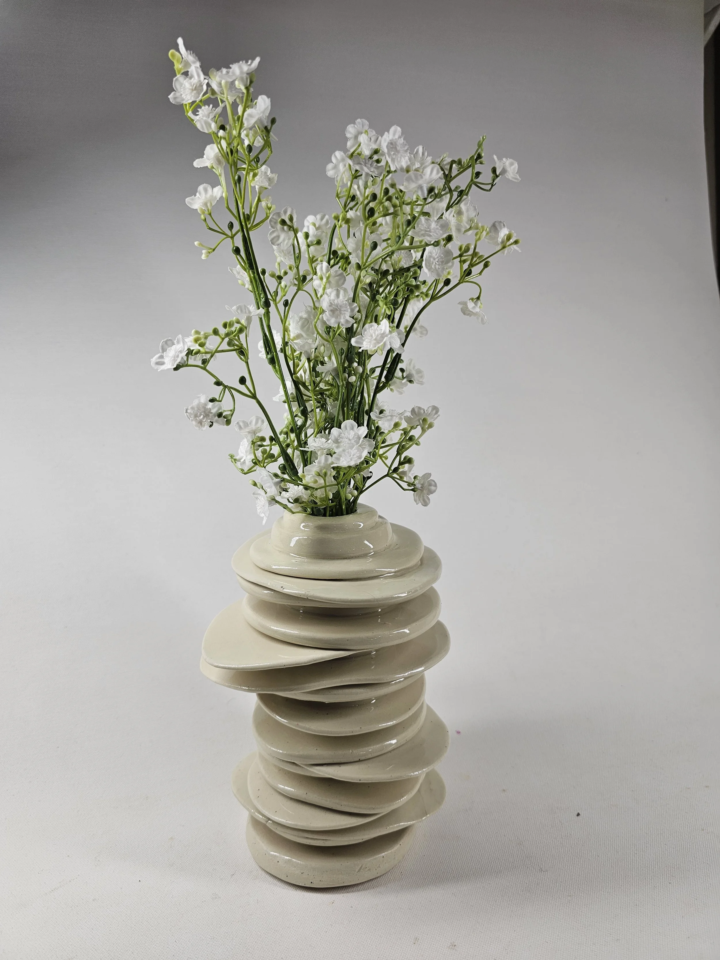 A ceramic vase with a stacked, layered design holding white artificial flowers with green stems and small blossoms.