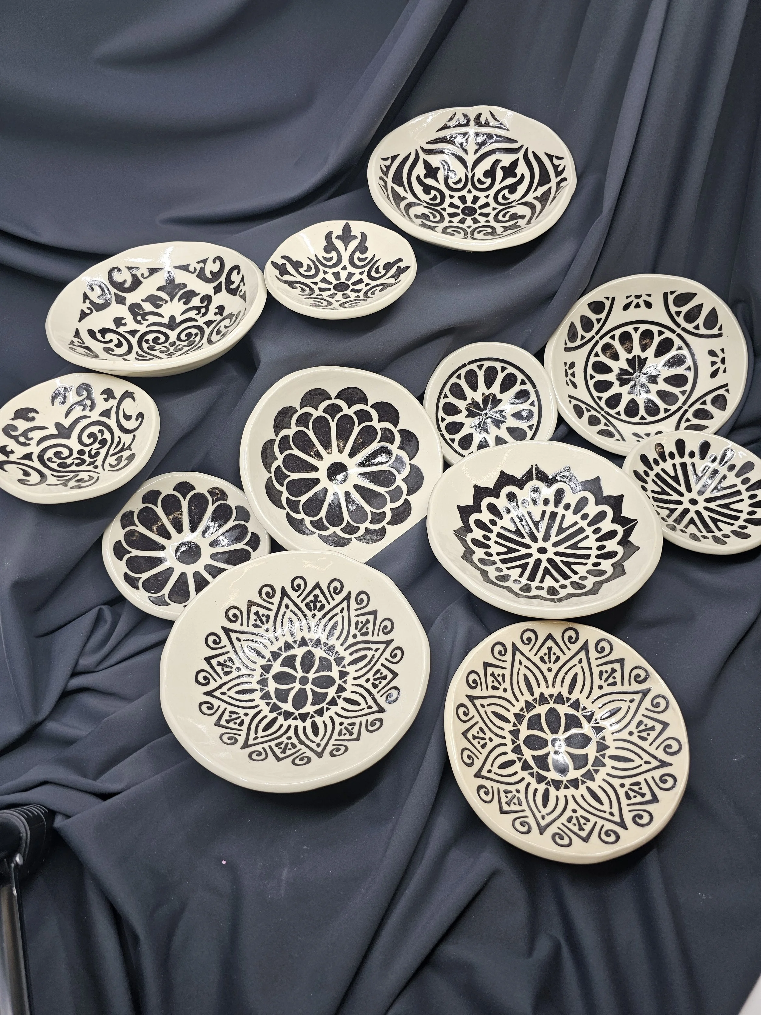 Collection of decorative black and white ceramic plates with intricate patterns, arranged on dark fabric.