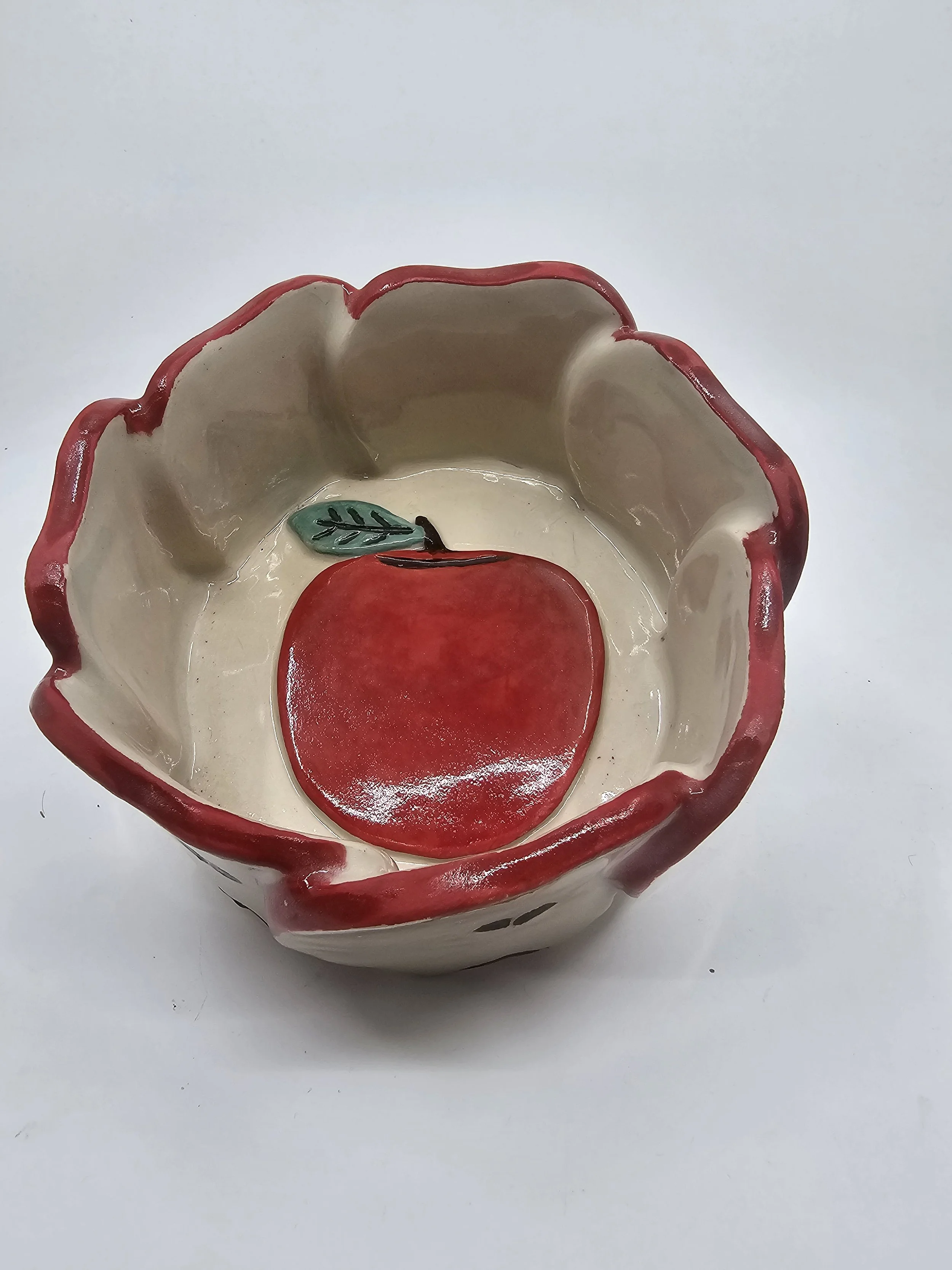 Decorative ceramic bowl with a red apple and a green leaf inside.