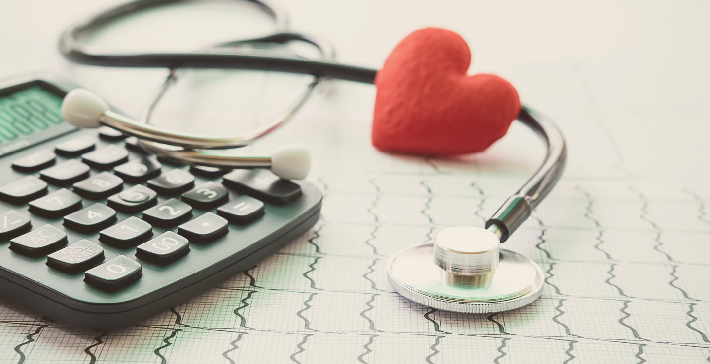 A stethoscope, a calculator, and a red heart shaped object placed on an electrocardiogram chart.