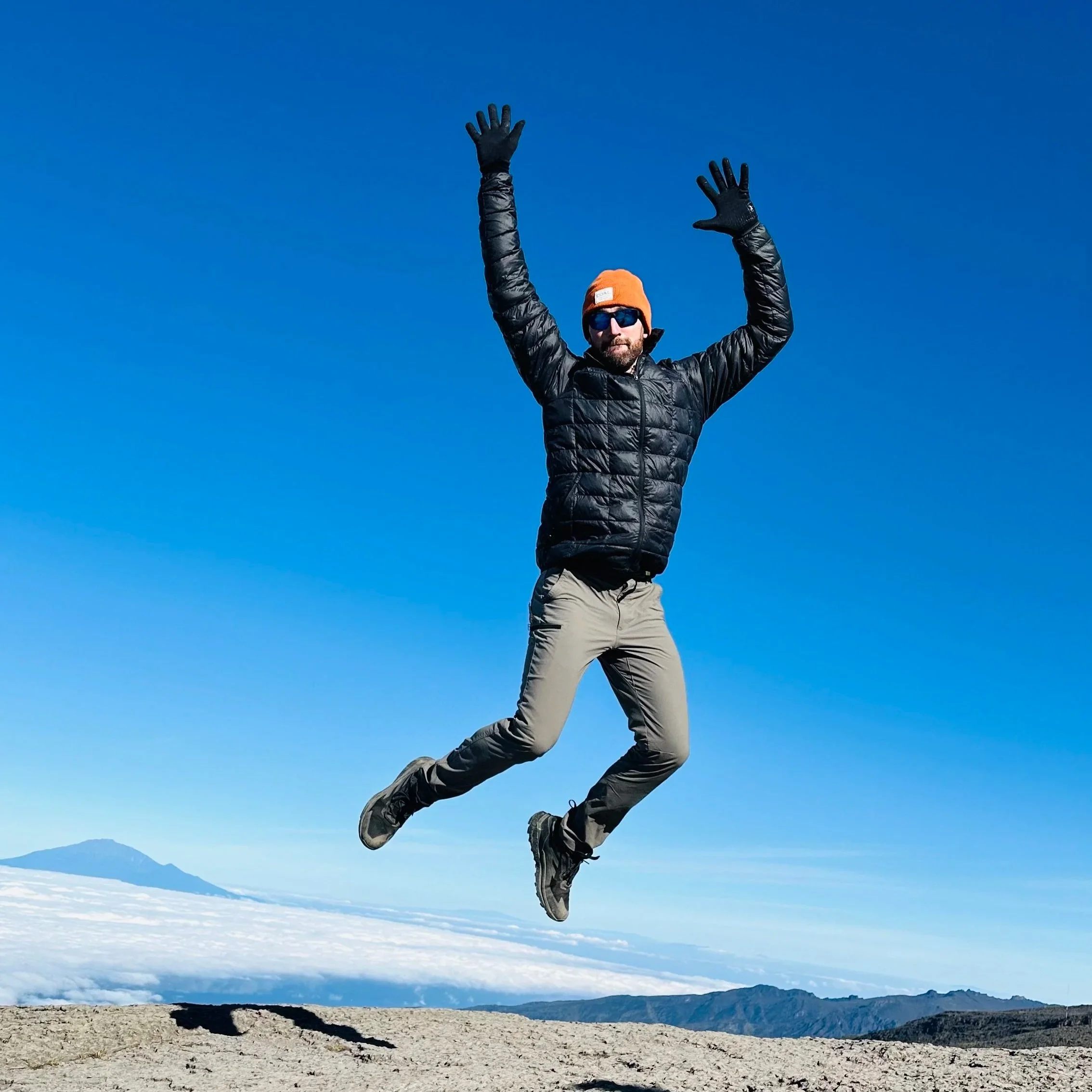 Man jumping in the air on a mountain with a clear blue sky and clouds in the background