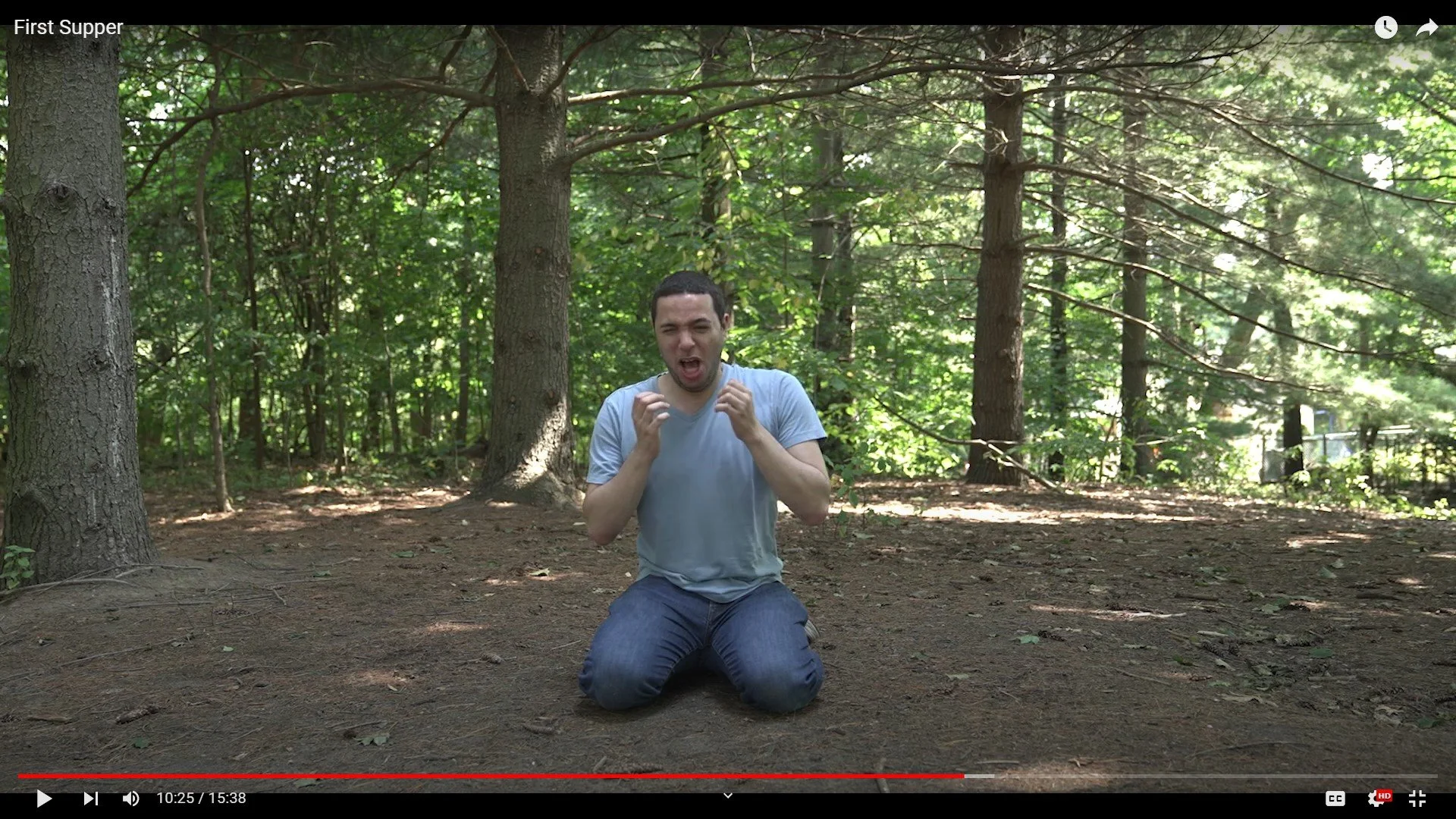A man kneeling on the ground in a forest, appearing distressed or upset, with forest trees and greenery in the background.