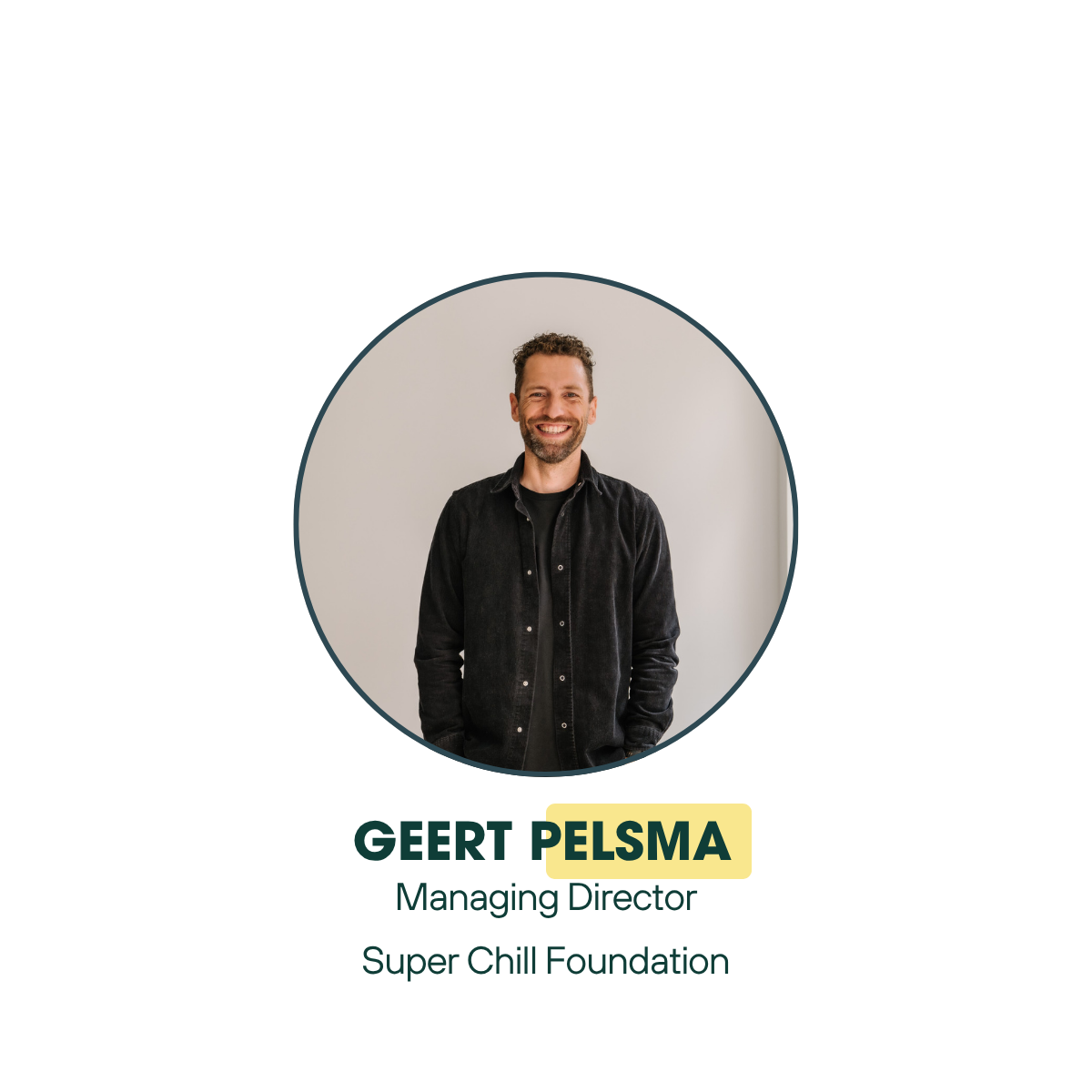 A smiling man with short curly hair and a beard, wearing a black shirt, standing against a plain light-colored wall.