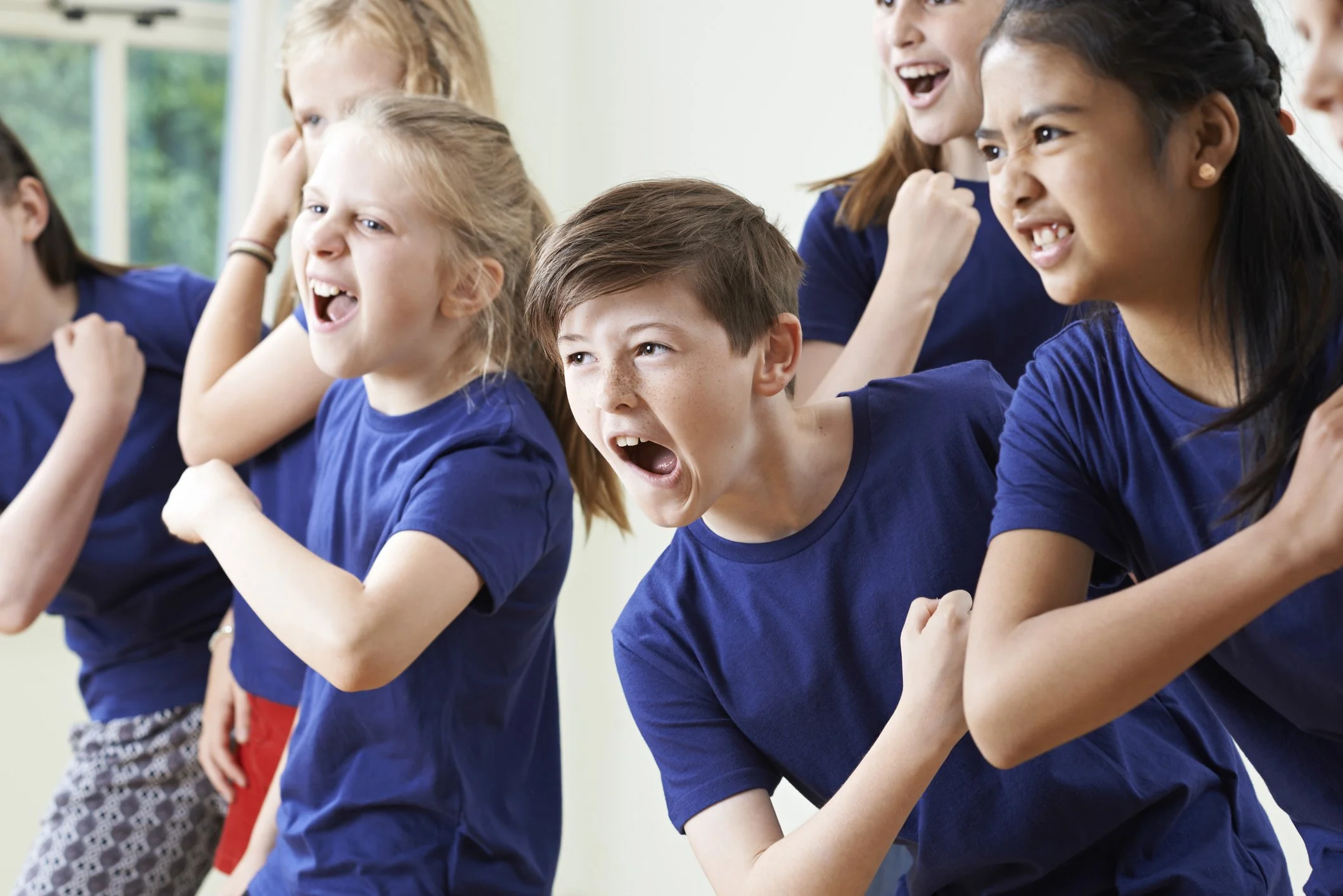A group of children and a young woman engaged in a fun activity, all wearing blue shirts and appearing to be laughing and enjoying each other's company.