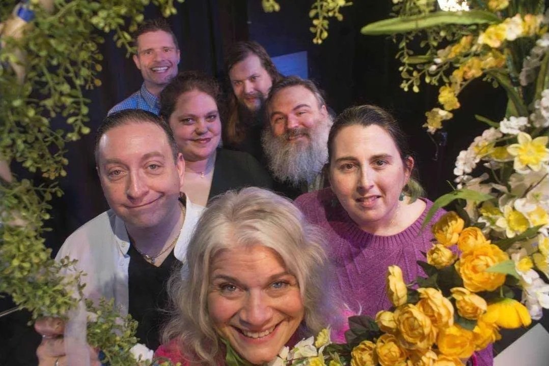 Members of The Regulars smiling at the camera, surrounded by yellow and white flowers, in a festive setting.