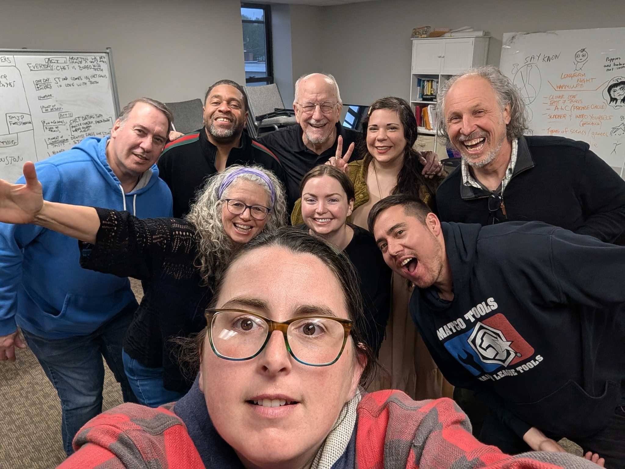 Members of Down the Rabbit Hole smiling taking a selfie in an indoor office, with whiteboards filled with notes in the background.
