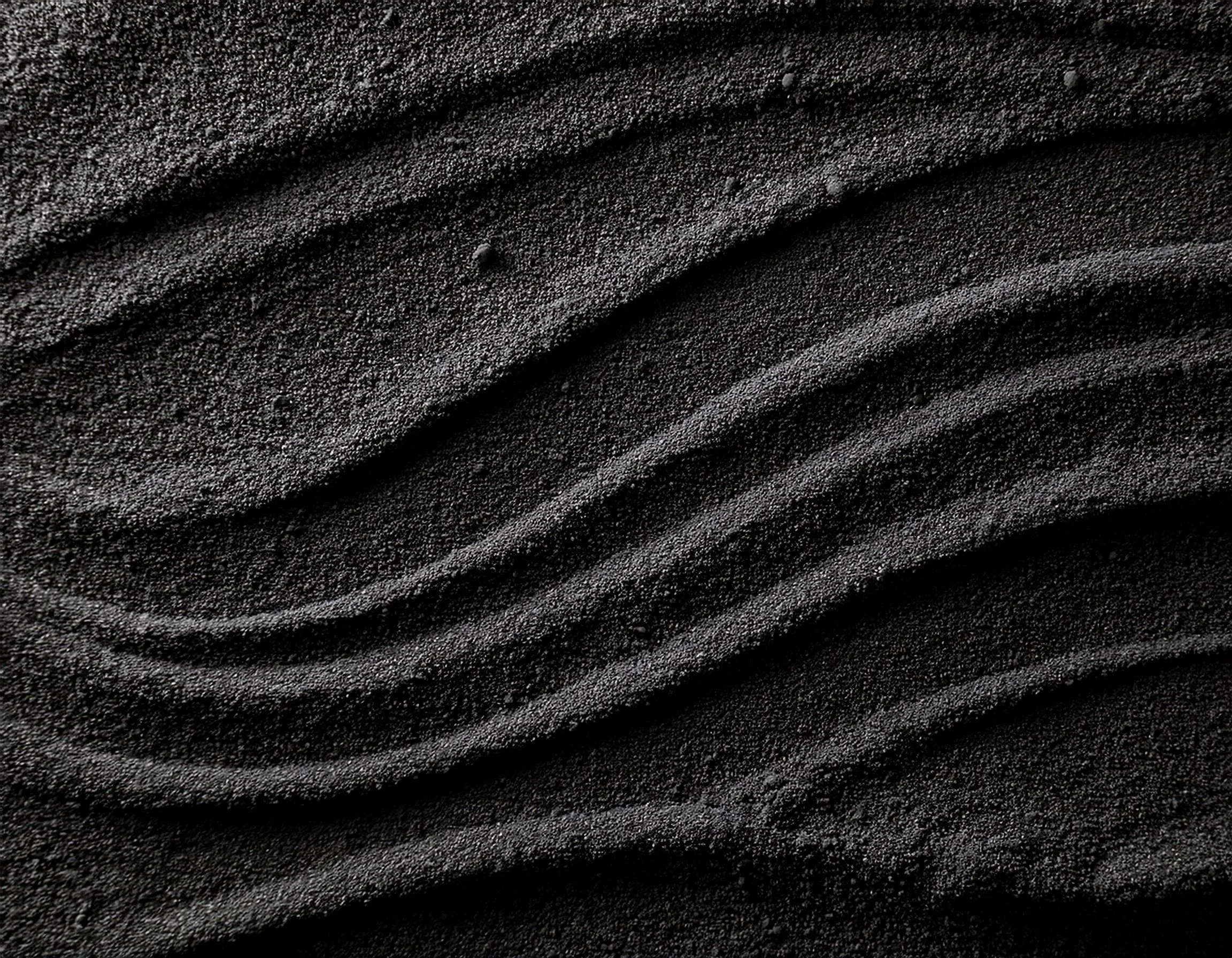 Close-up of black sand with parallel ridges and fine grains.