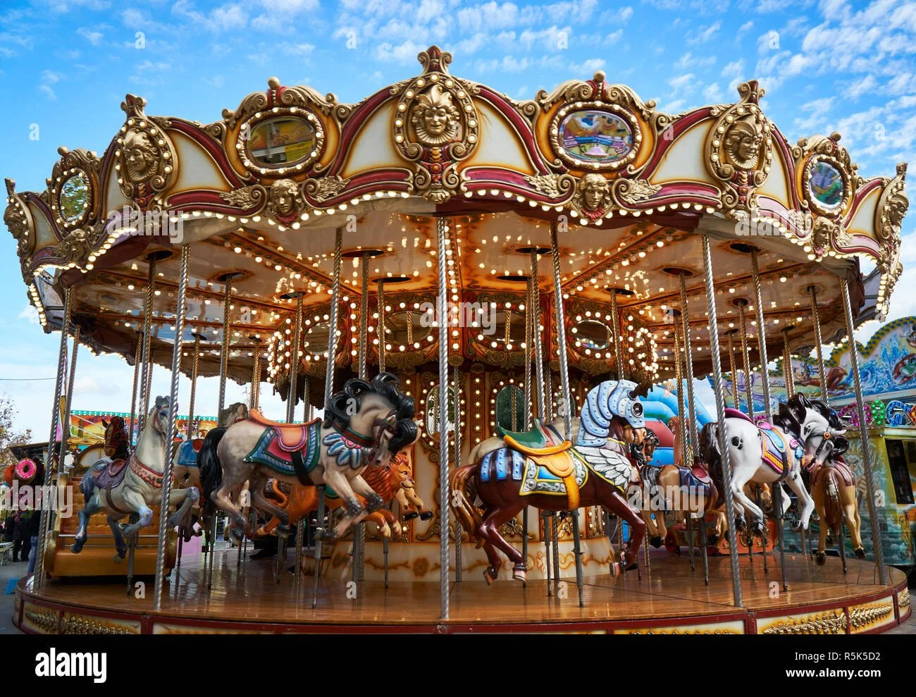 Colorful vintage carousel with painted horses rides at a fair under a partly cloudy sky.