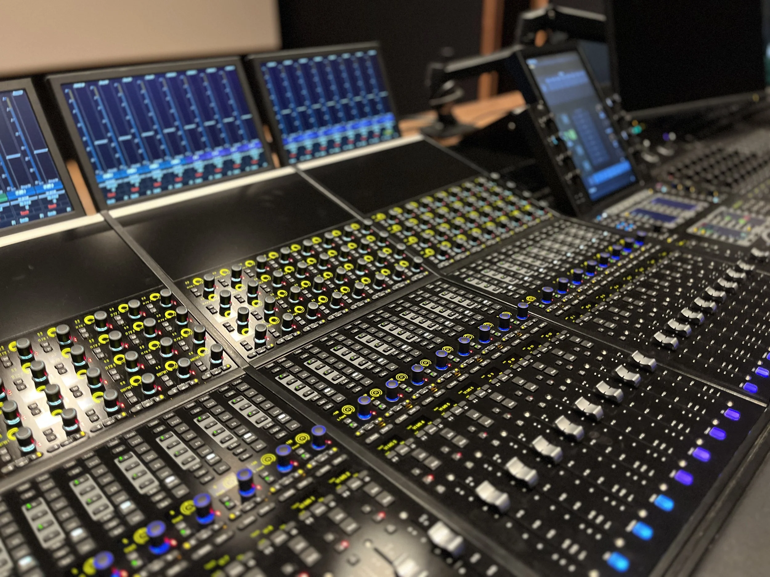 Table de mixage audio avec plusieurs écrans et nombreux boutons lumineux.