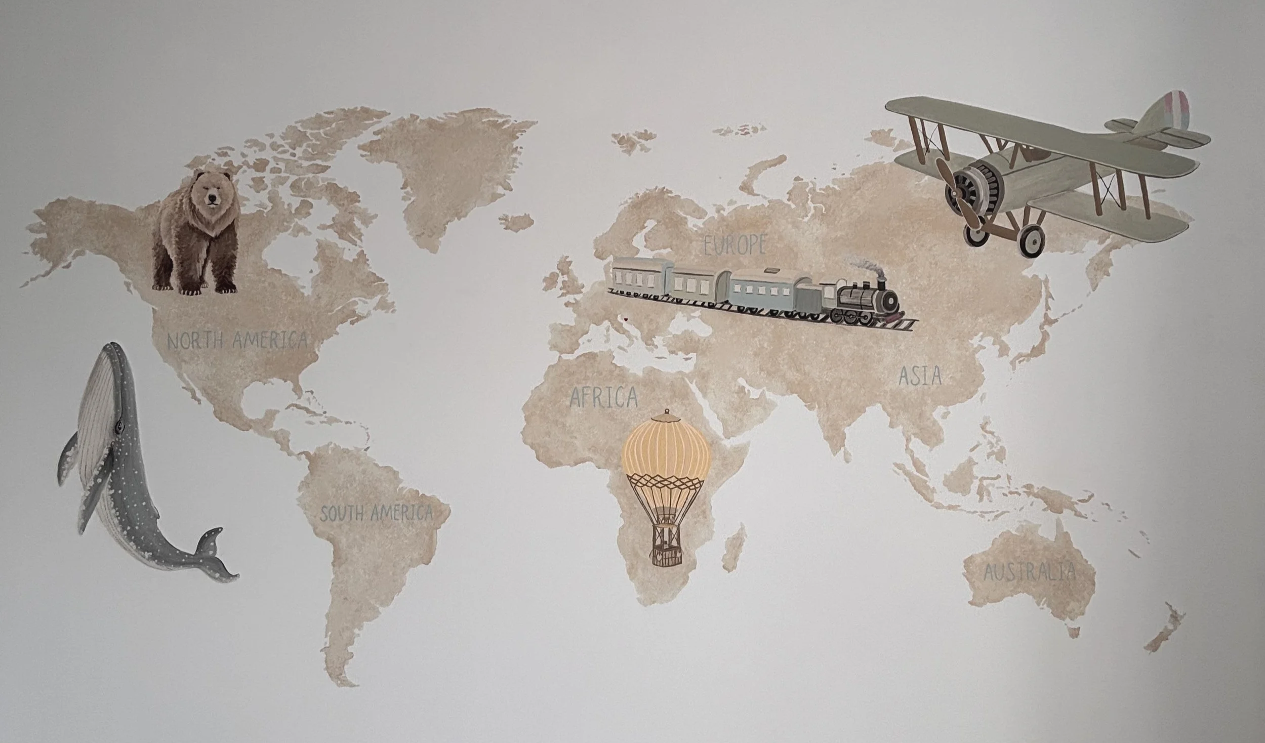 hand painted world map wall mural. inspire adventure and curiosity. educatinal settings. mural artist hertfordshire. trains, planes, hot air balloon, whale, bear. meaningful art for kids room. natural habitat. bespoke mural, school mural. office art.