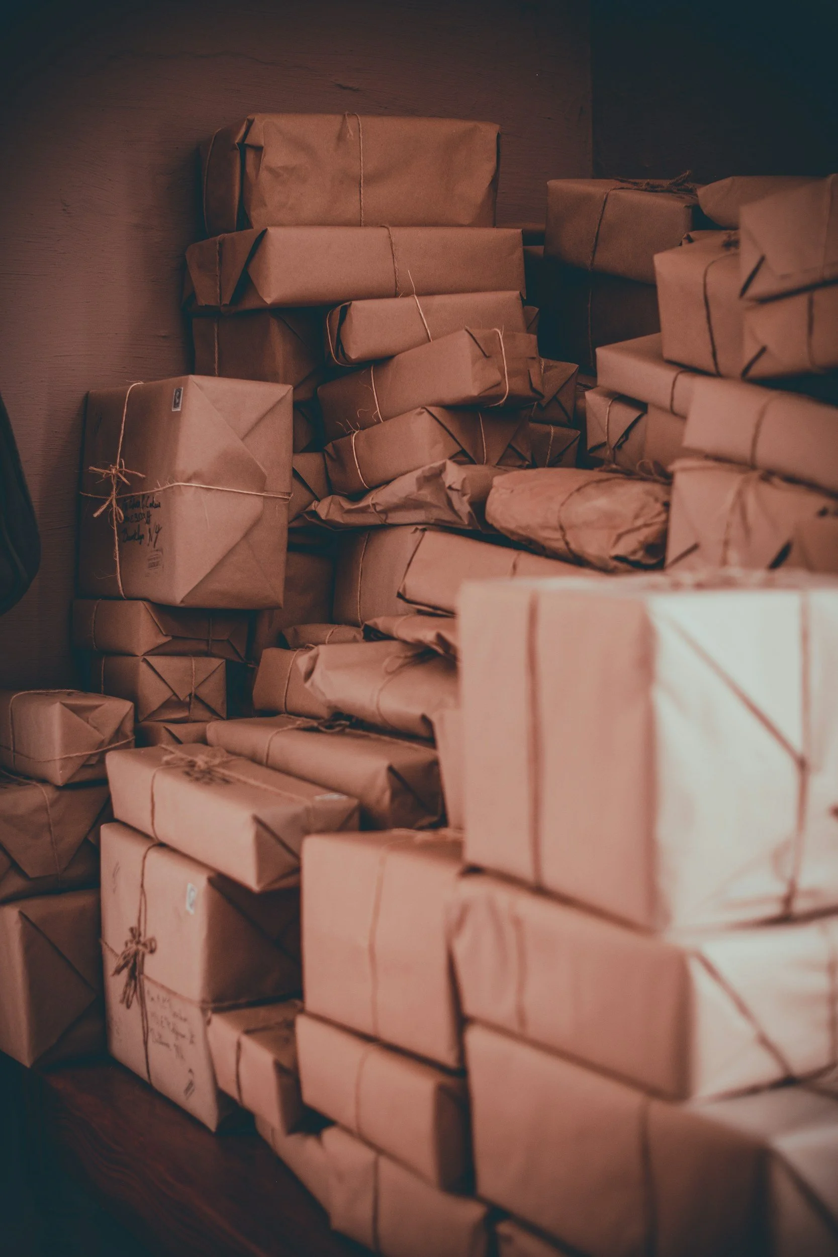 A stack of parcels wrapped in brown paper and tied with string, arranged on a wooden surface.