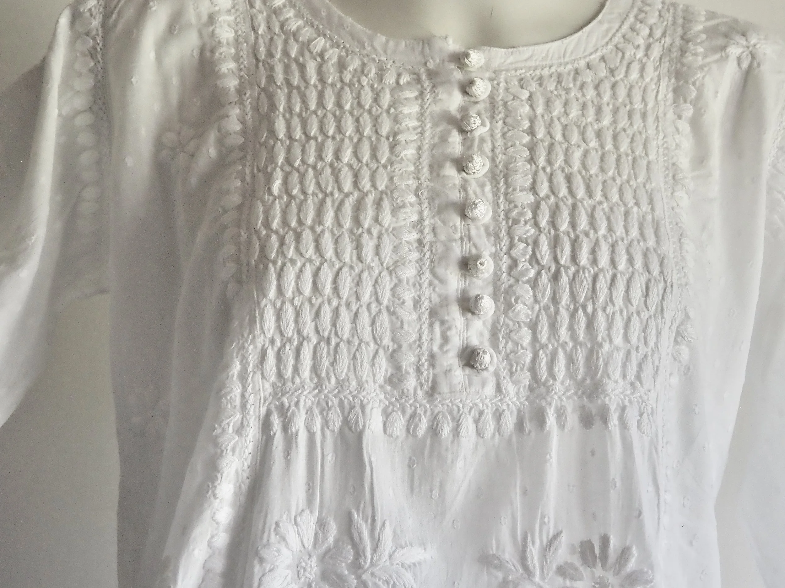 White blouse or dress with embroidered details and buttons on the front, made of shiny fabric.