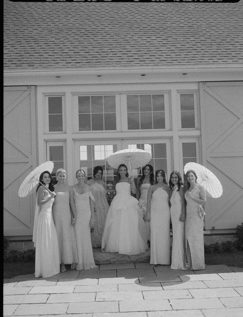 Group of women in formal dresses standing outside in front of a barn-style building.