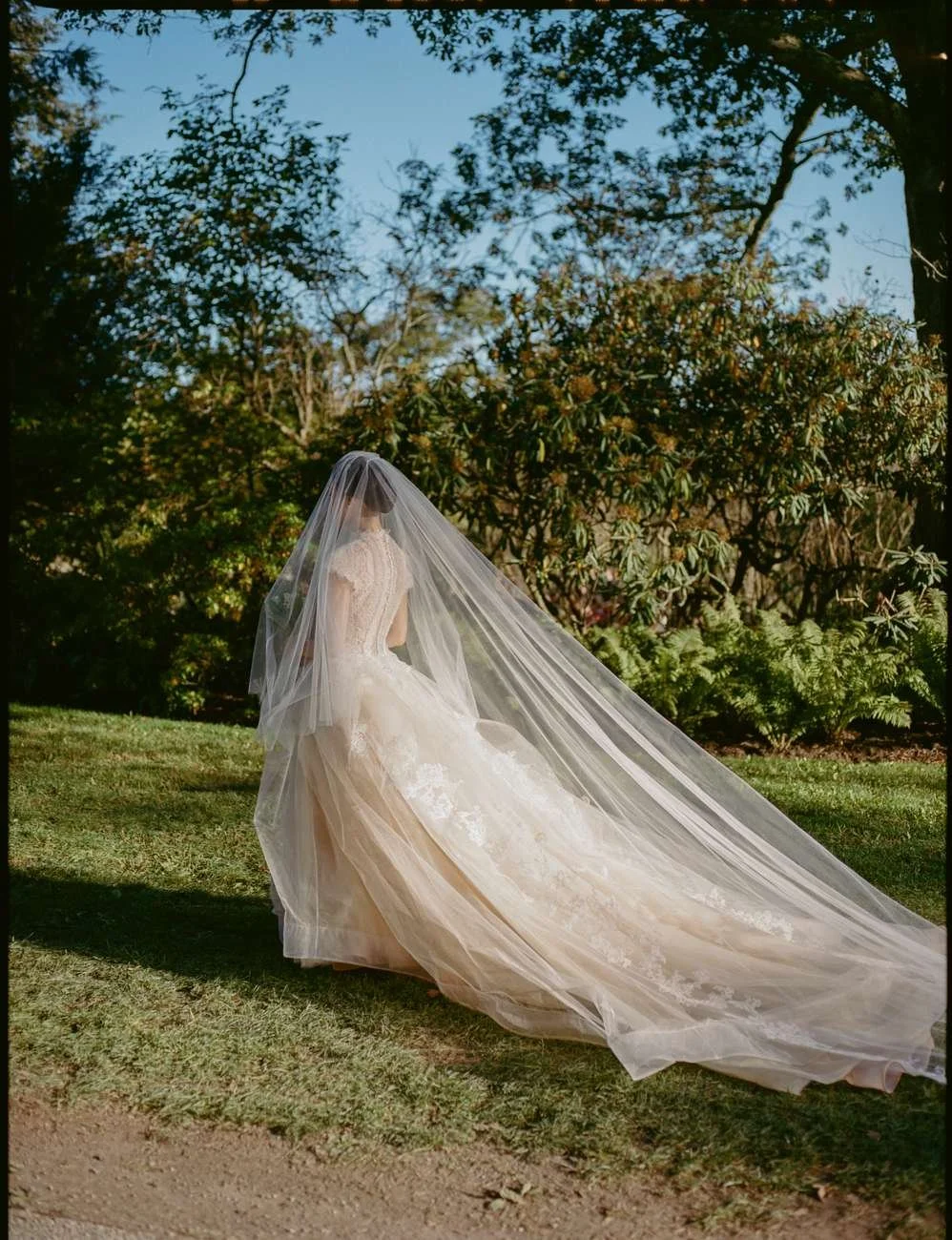 A bride in a wedding dress with a long veil standing outdoors.