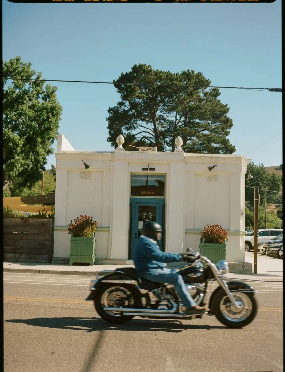 A man riding a motorcycle past a white building under a clear blue sky.