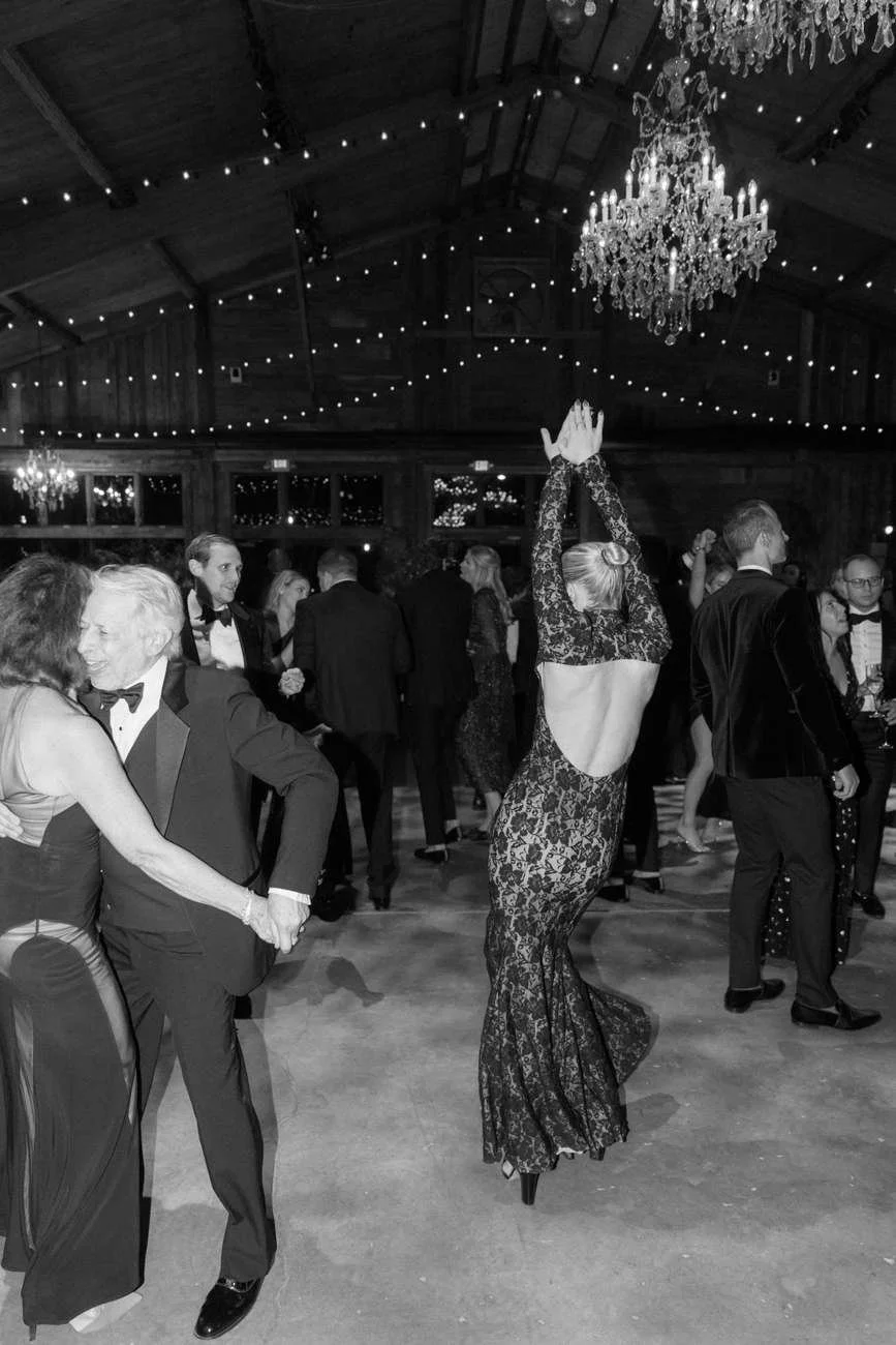 People dancing and socializing at an elegant event in a decorated hall with chandeliers and string lights.