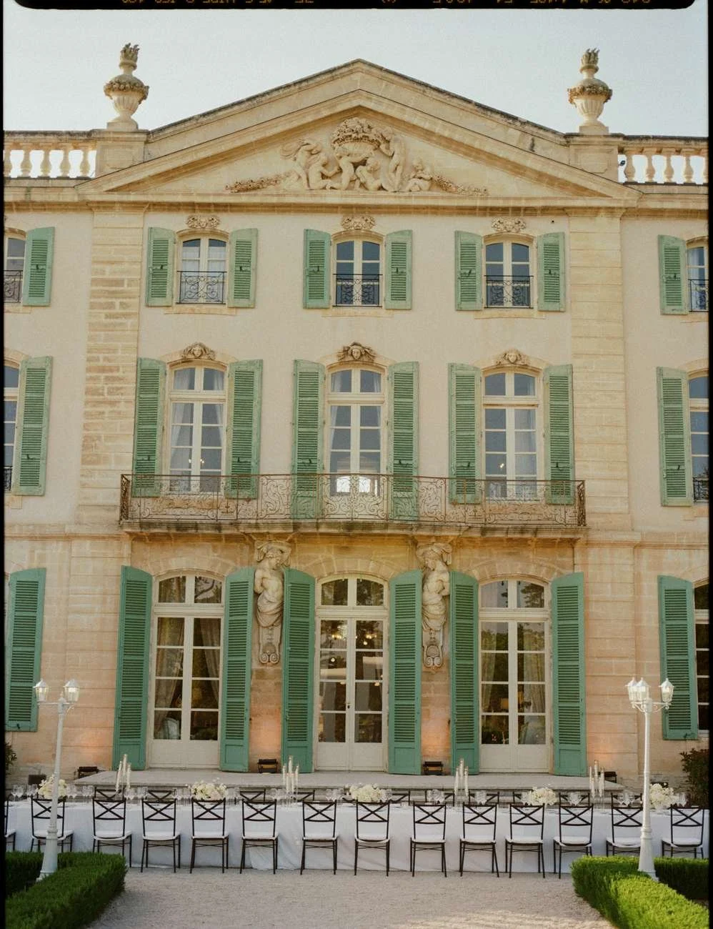 Elegant multi-story mansion with tall windows and green shutters, set up for an outdoor event.