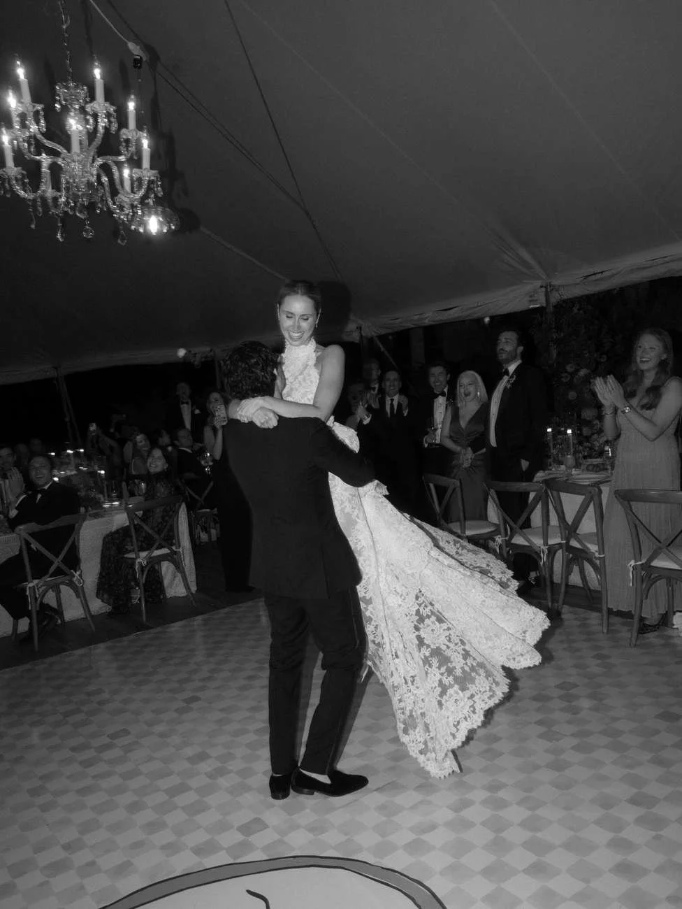 A couple dancing at a wedding reception, with the bride in a white gown lifted in the air by the groom.