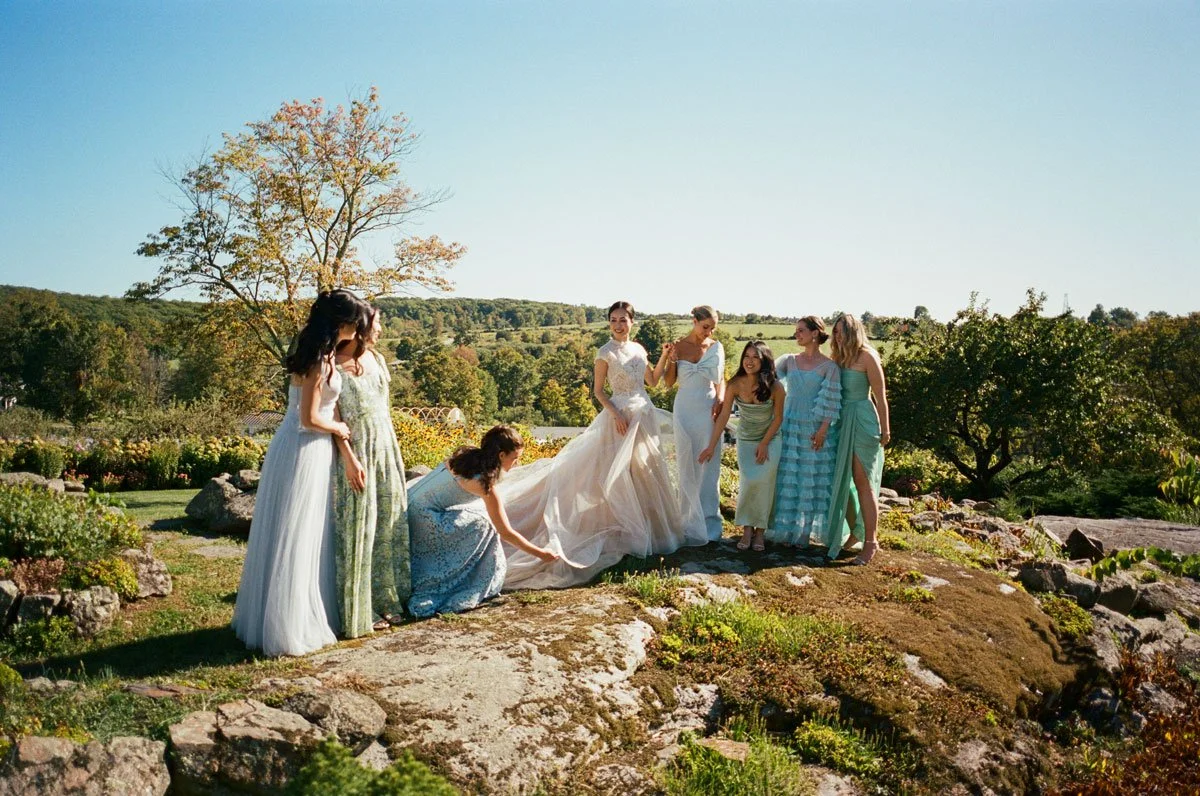 A group of women in colorful dresses gathered outdoors, in a scenic garden setting.