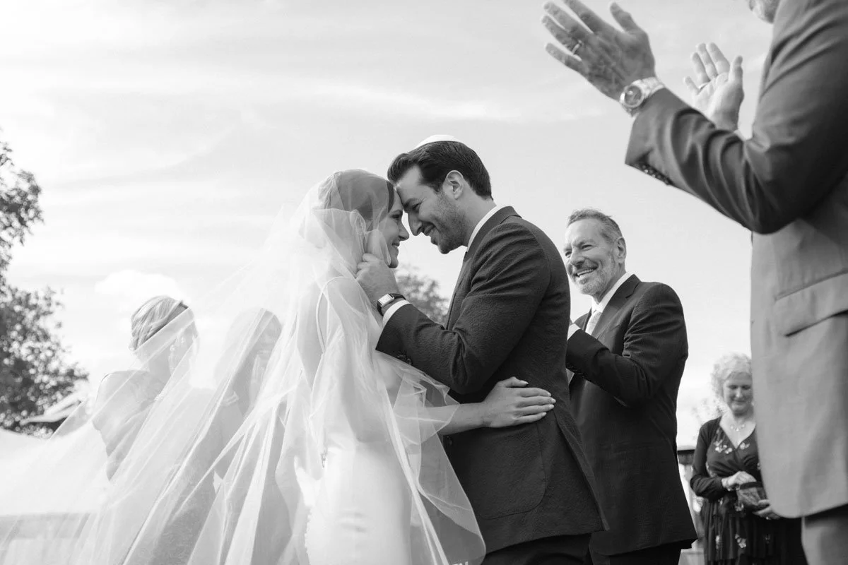 A bride and groom touch foreheads and smile during their outdoor wedding ceremony.