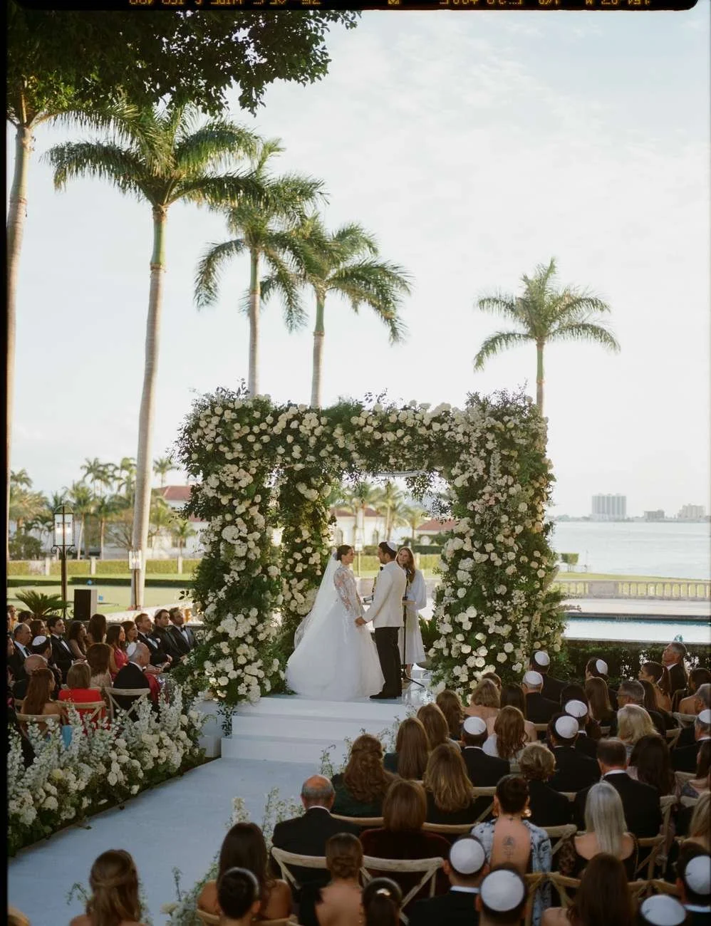 A wedding ceremony with the bride and groom standing under a floral arch.