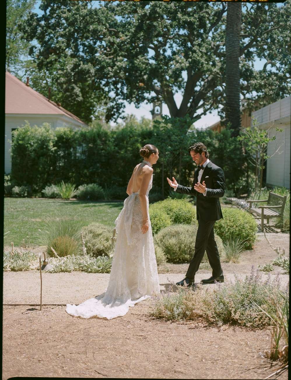 A bride and groom in formal wedding attire in a garden, engaging in a joyful moment.