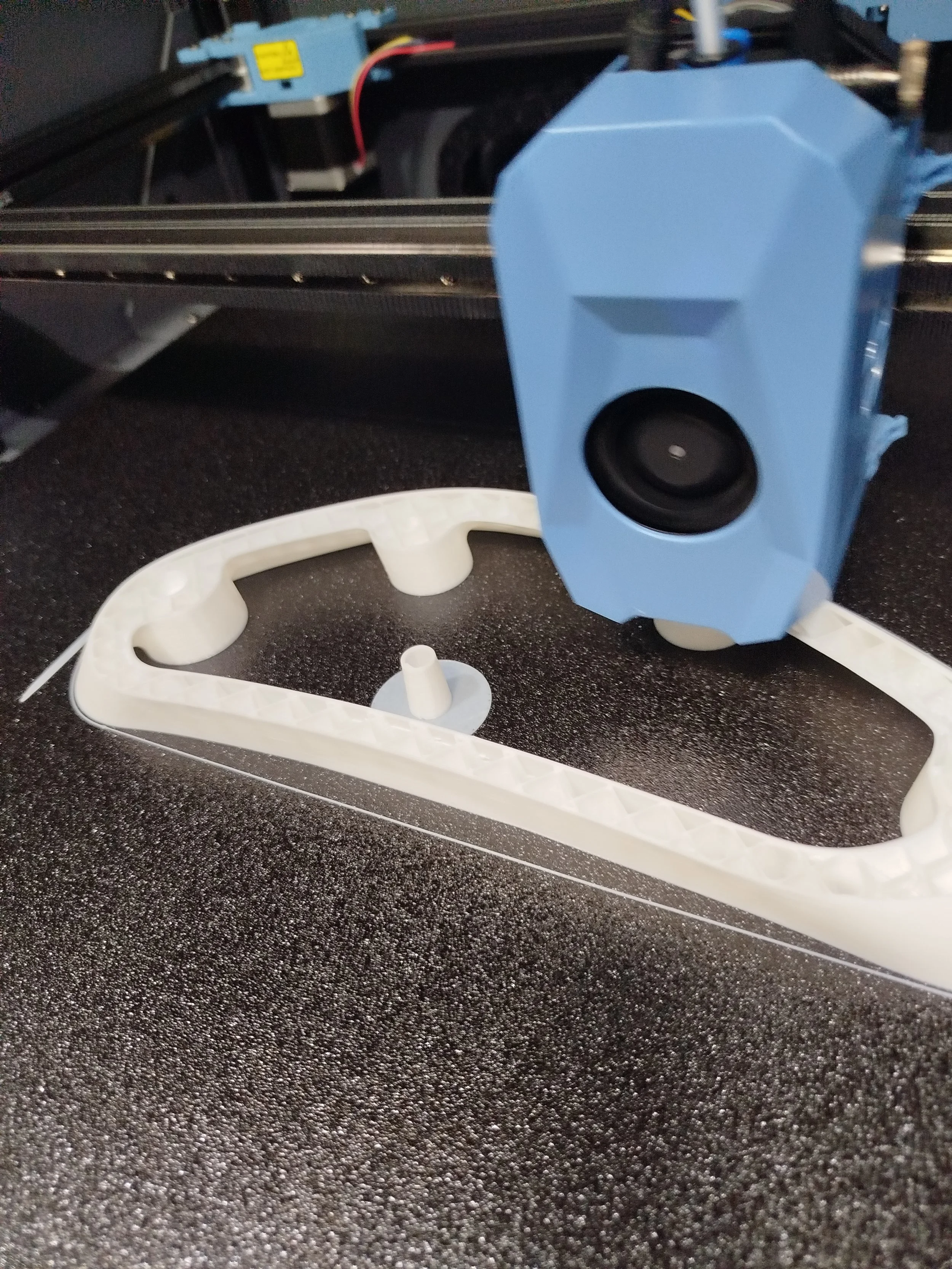Une imprimante 3D en cours d'utilisation avec une pièce en plastique blanc en cours de fabrication sur la surface noire de l'imprimante.