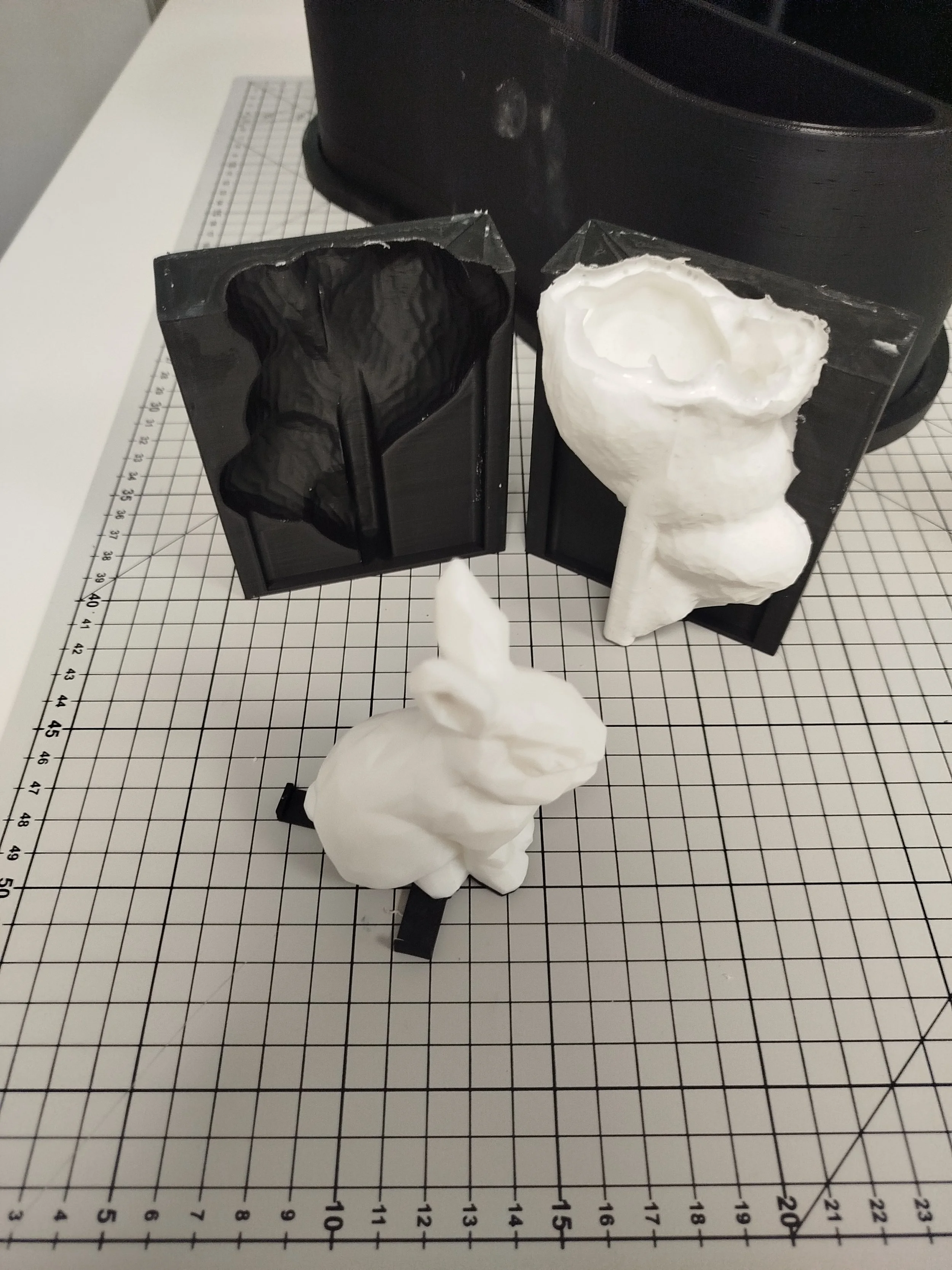 Moules en silicone avec  figurine en résine d’un animal (lapin ou autre) en cours de fabrication, posés sur une surface à carreaux avec un fond noir.