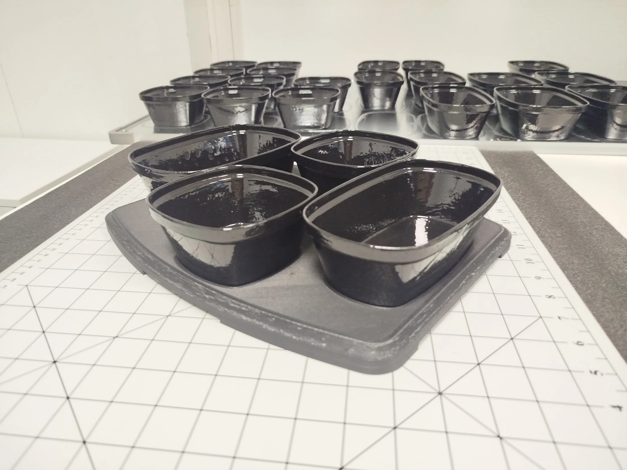 Petits récipients noirs en silicone sur une surface de travail avec un tapis de coupe, utilisés pour la cuisson ou la pâtisserie.
