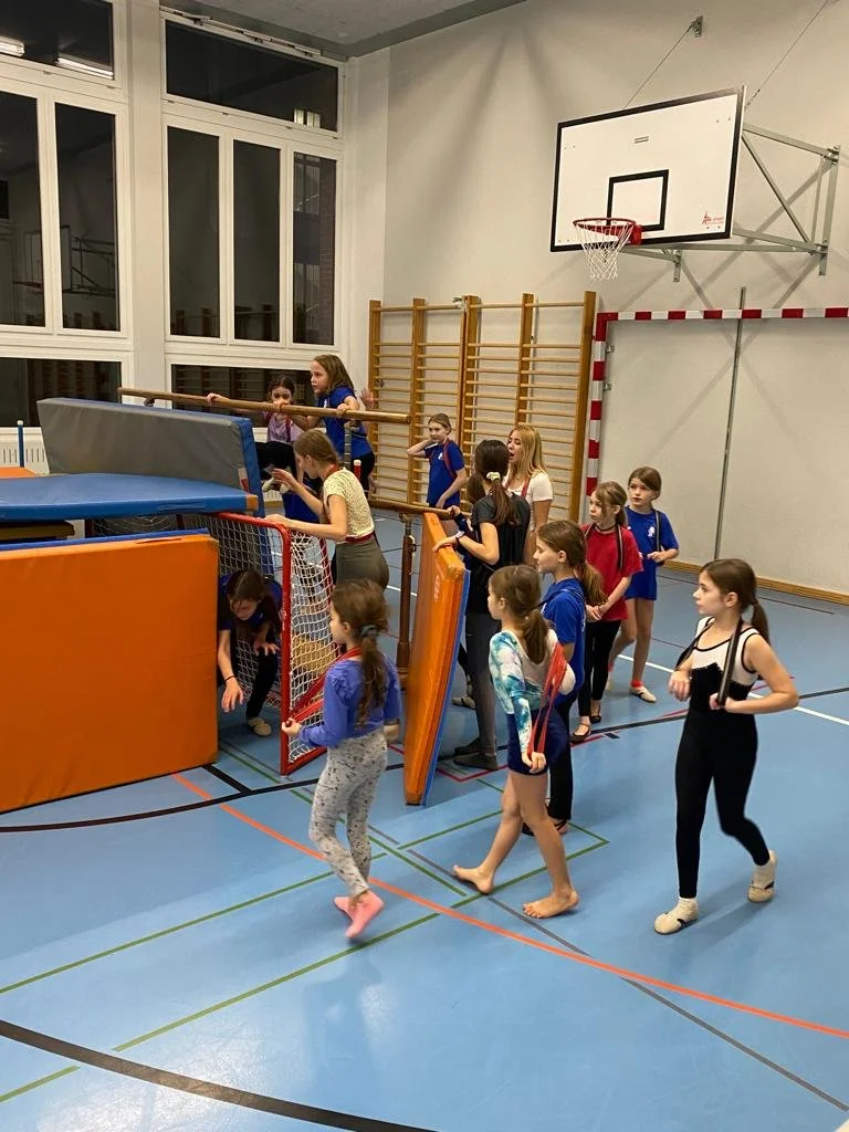 Kinder in einer Turnhalle warten in einer Schlange auf das Klettern an einem Klettergerüst.