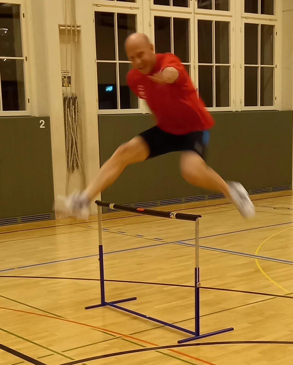 Ein Mann springt über einen kleinen Hindernis in einer Turnhalle.