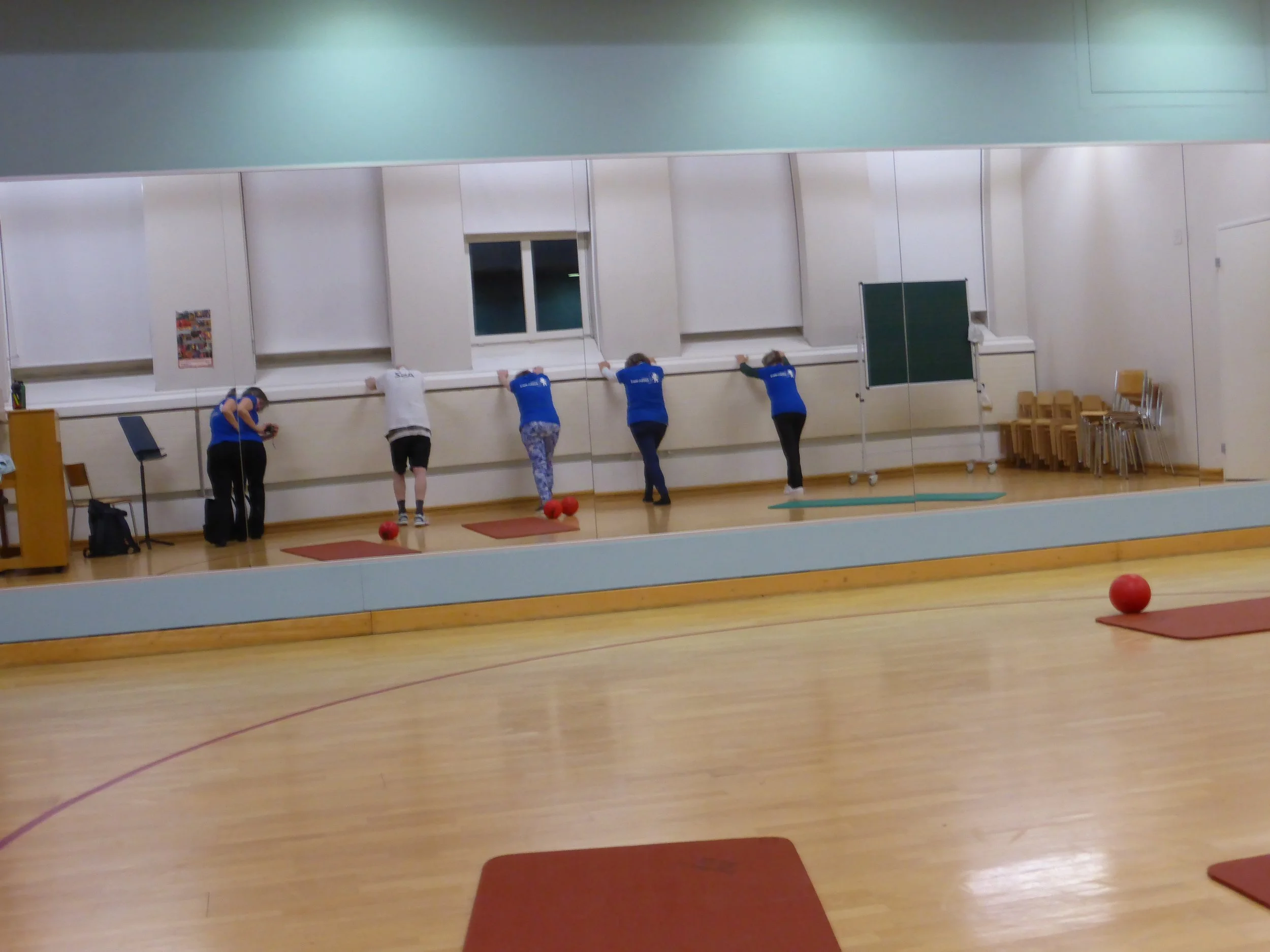 Fünf Menschen trainieren in einem Fitnessraum mit Spiegel, einige lehnen am Fenster, während sie auf den Antwortkreislinien stehen und trainieren, während rote Bälle auf den Matten liegen.