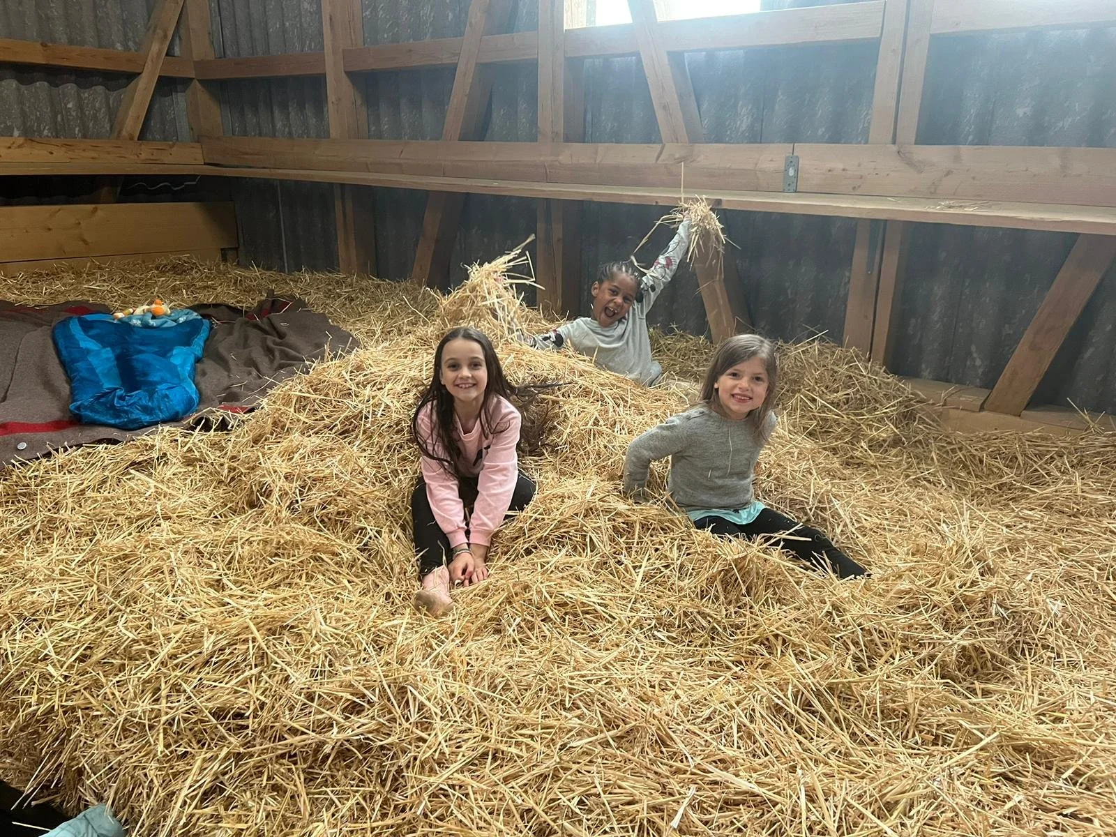 Drei lachende Kinder spielen in Heu in einer Scheune.