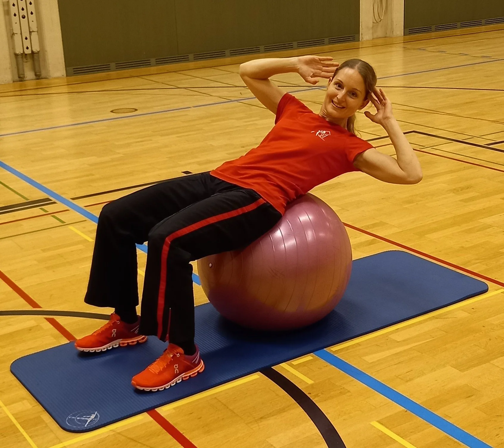 Frau trainiert im Fitnessstudio mit dem auf einem Gymnastikball auf einer Matte liegend, in sportlicher Kleidung und mit einer Handhaltung.