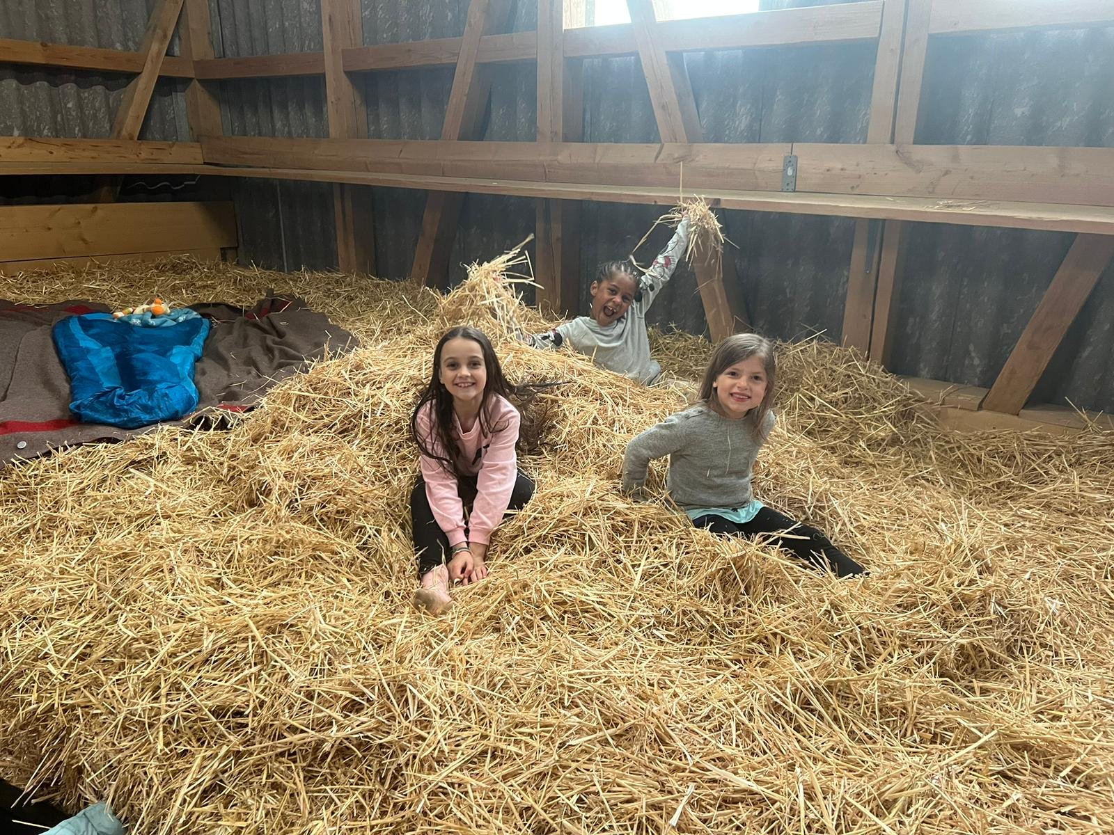 Drei Kinder spielen in einem Heuhaufen im Heuhof. Sie lachen und haben Spaß.
