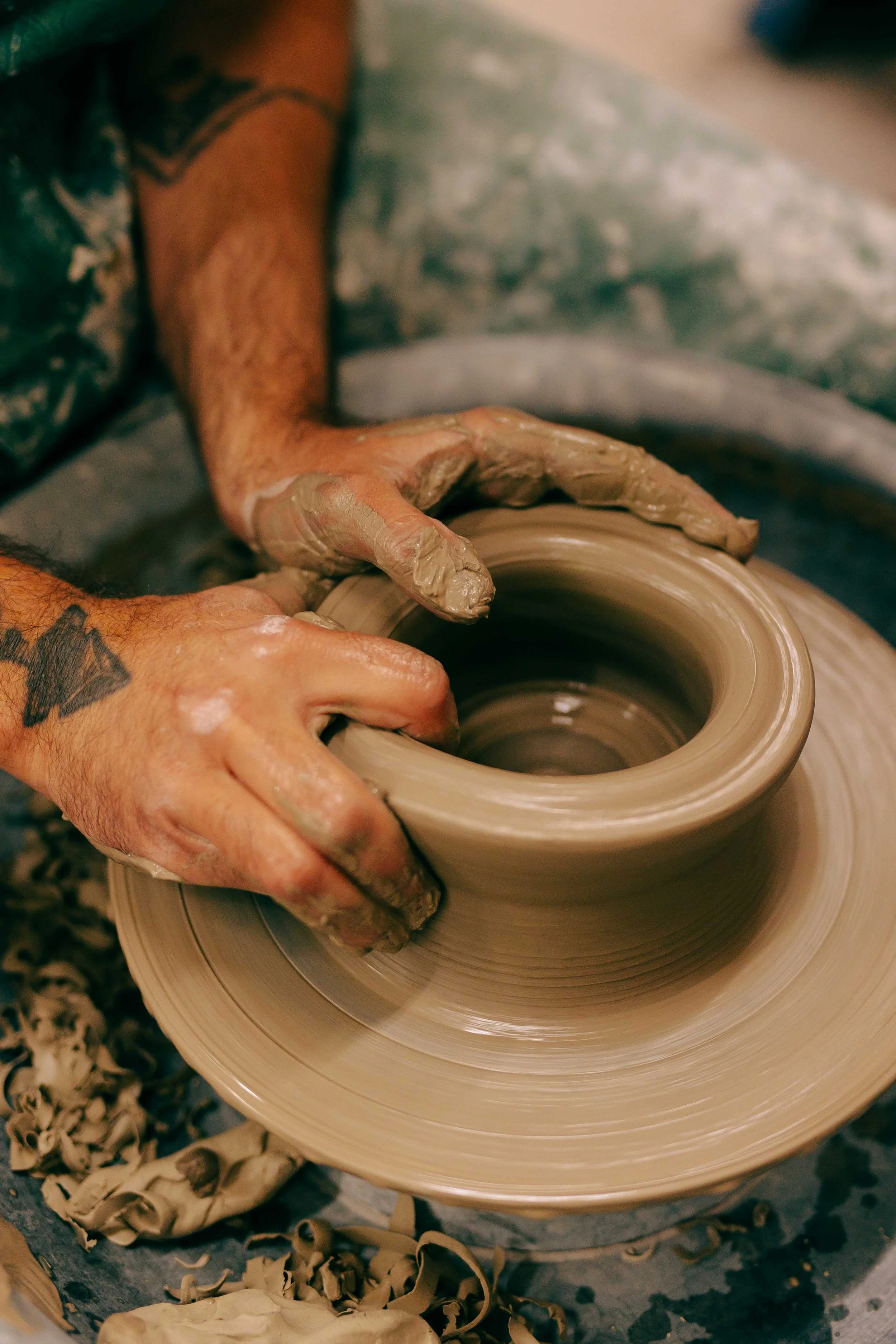 Hands shaping wet clay on a spinning pottery wheel in a pottery studio.