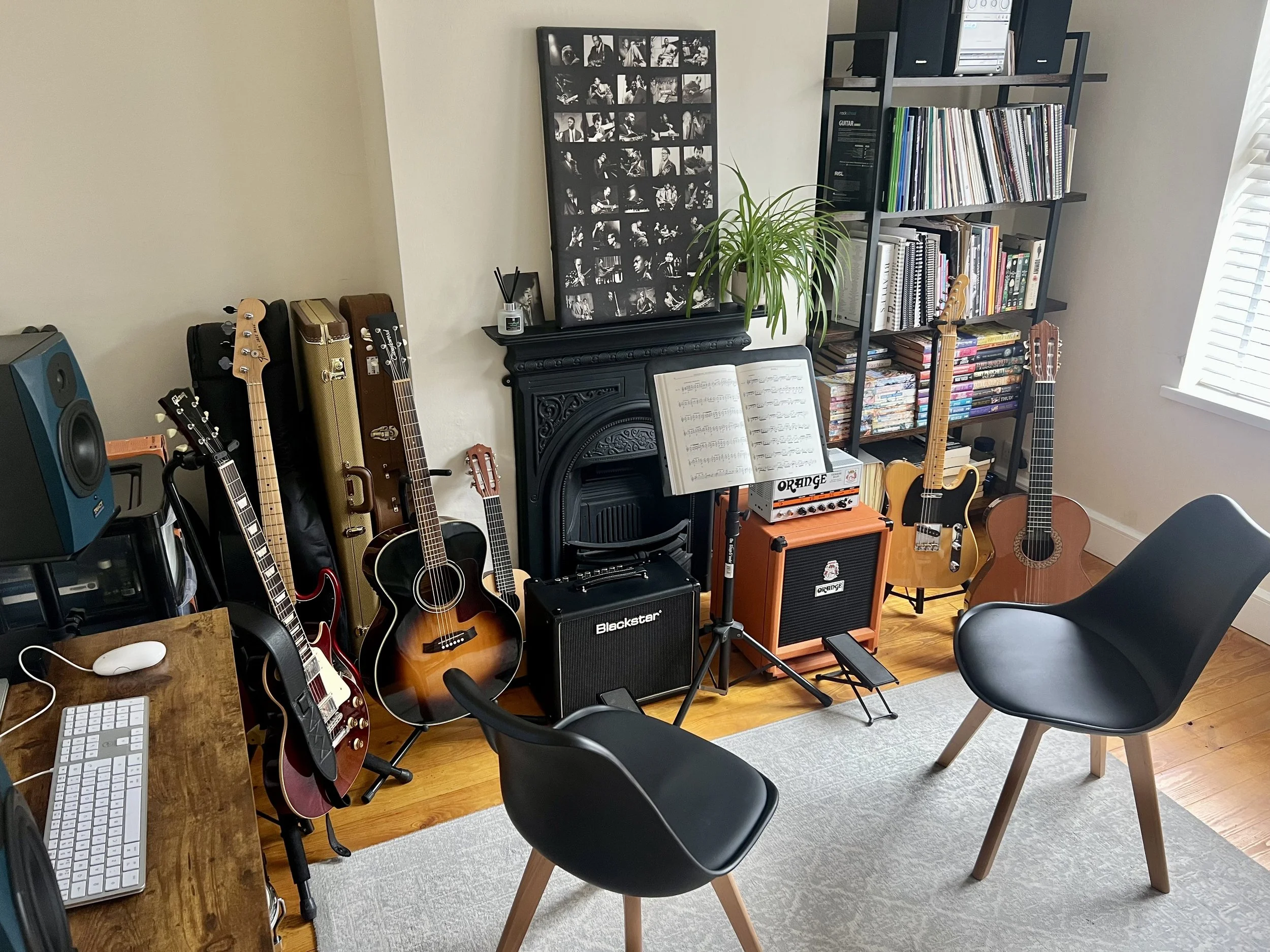 Music room with guitars, amplifier, music stand, bookshelves, and a computer on a wooden desk.