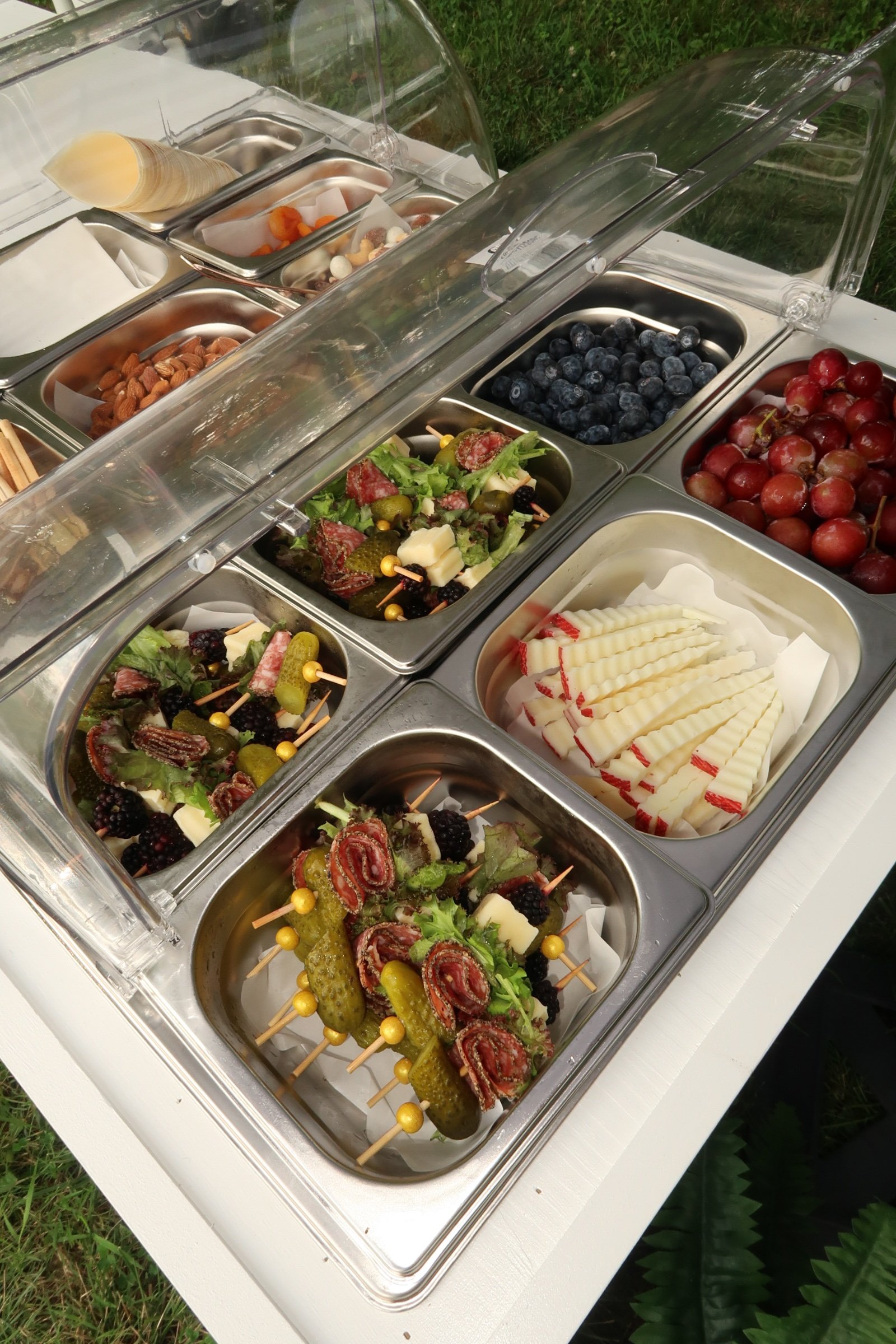 A snow cone stand with various flavor options and an assortment of fresh berries and fruit on skewers.