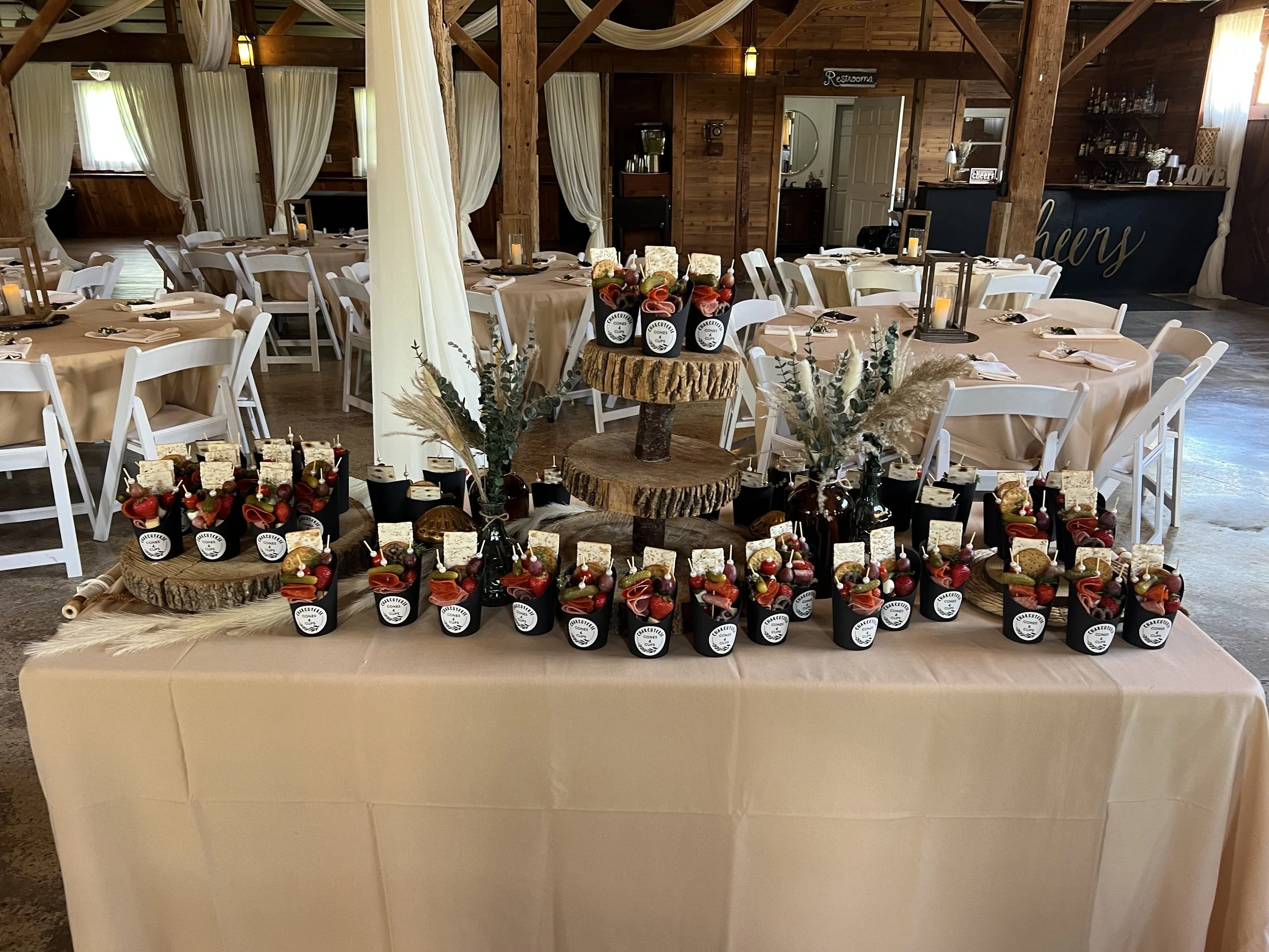 Tables set with beige tablecloths, candles, and flower arrangements in a rustic wooden venue decorated for a celebration or event.