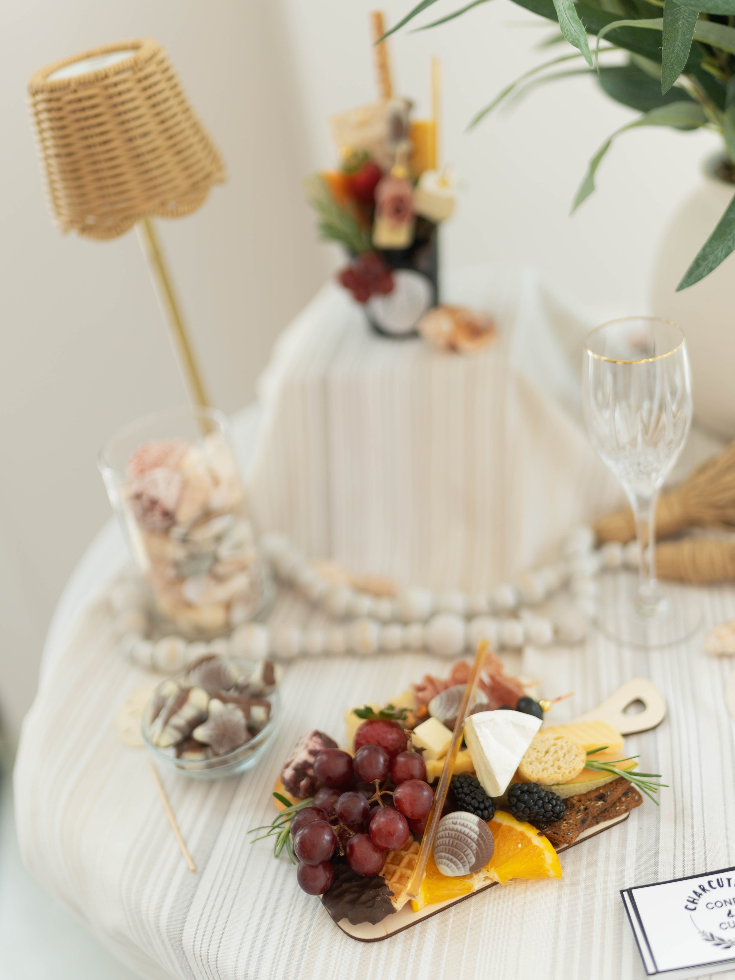 A charcuterie board with grapes, cheese, blackberries, and crackers, set on a white tablecloth with a wine glass nearby.