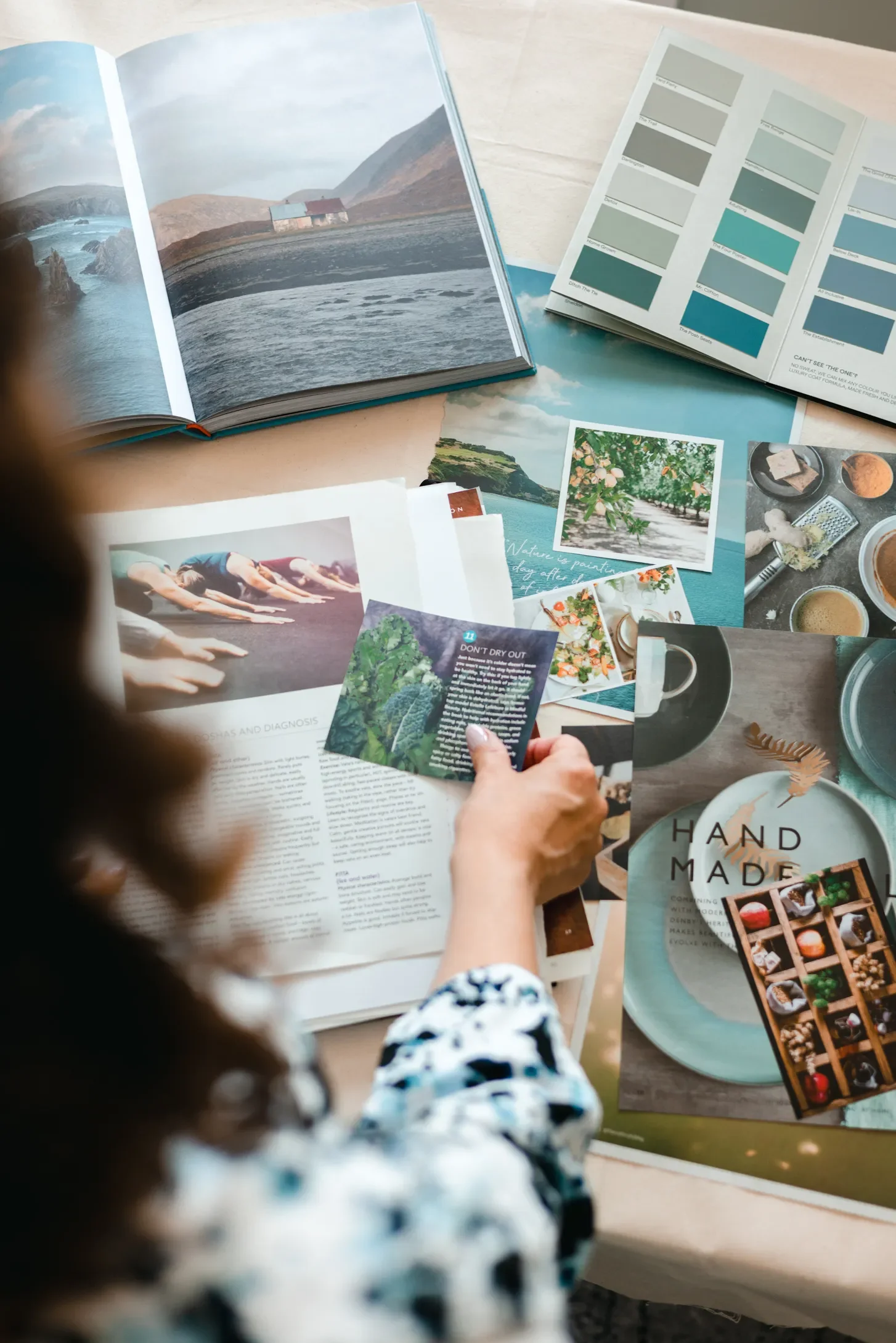 Brand designer Sammy Phillips looking at various magazine page cutouts and colour swatches lying on a table, gathering inspiration during a brand styling session