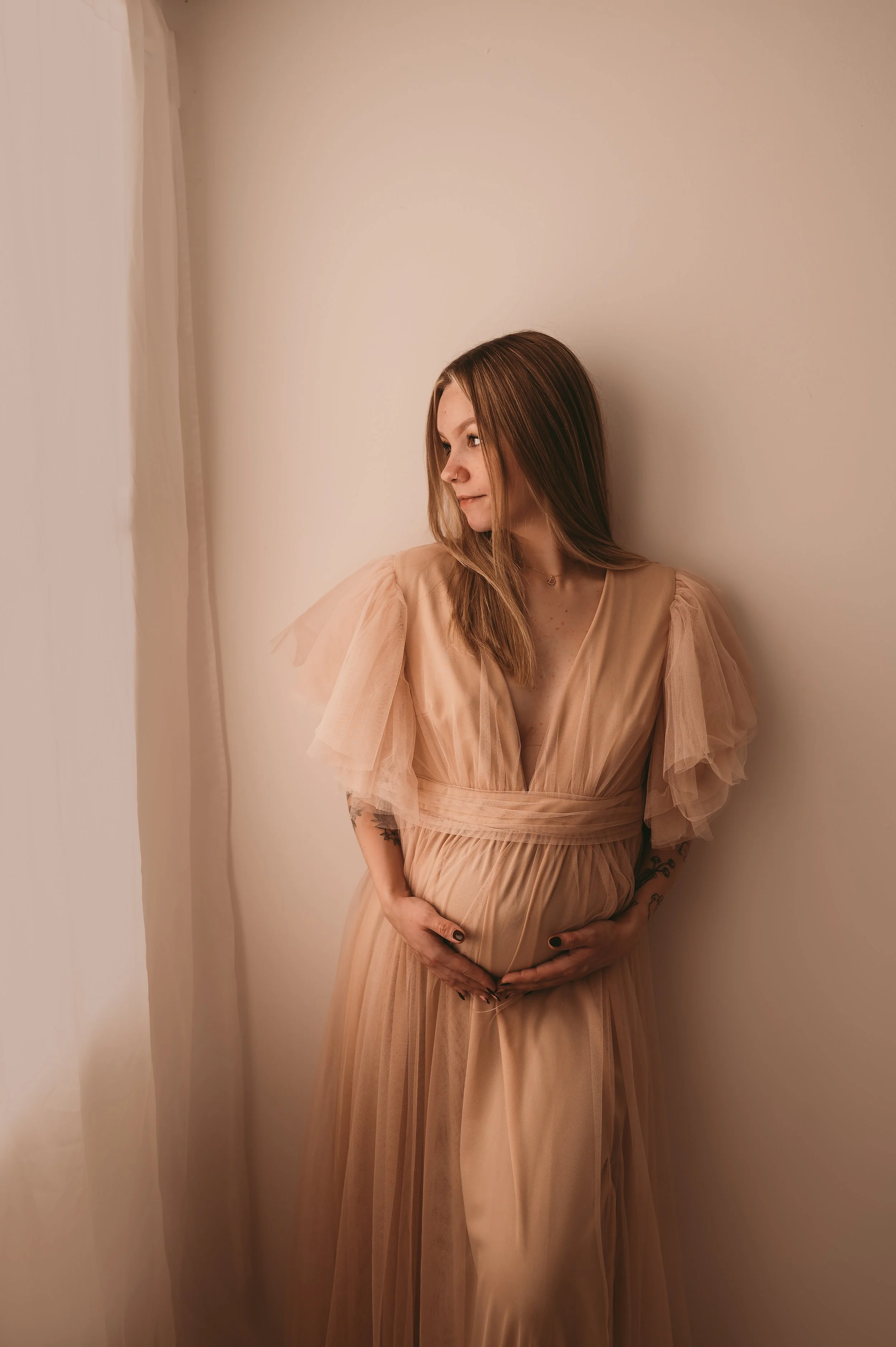 woman looking towards window light cuddling baby bump,  Maternity photography by kp-photo, based in Wiltshire