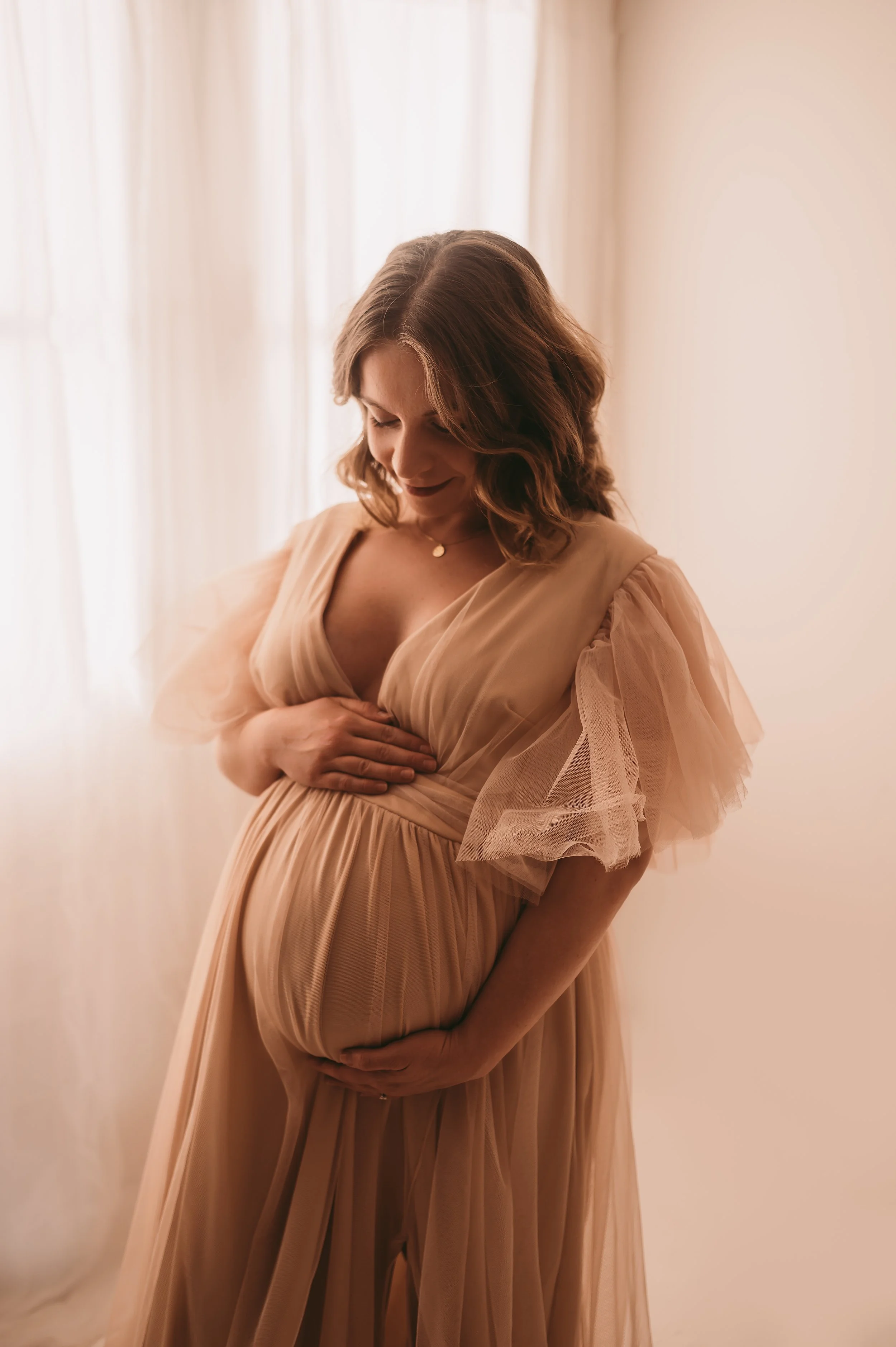 A Woman wearing a tulle dress posing for a photograph with her baby bump. Maternity photography by kp-photo, based in Wiltshire