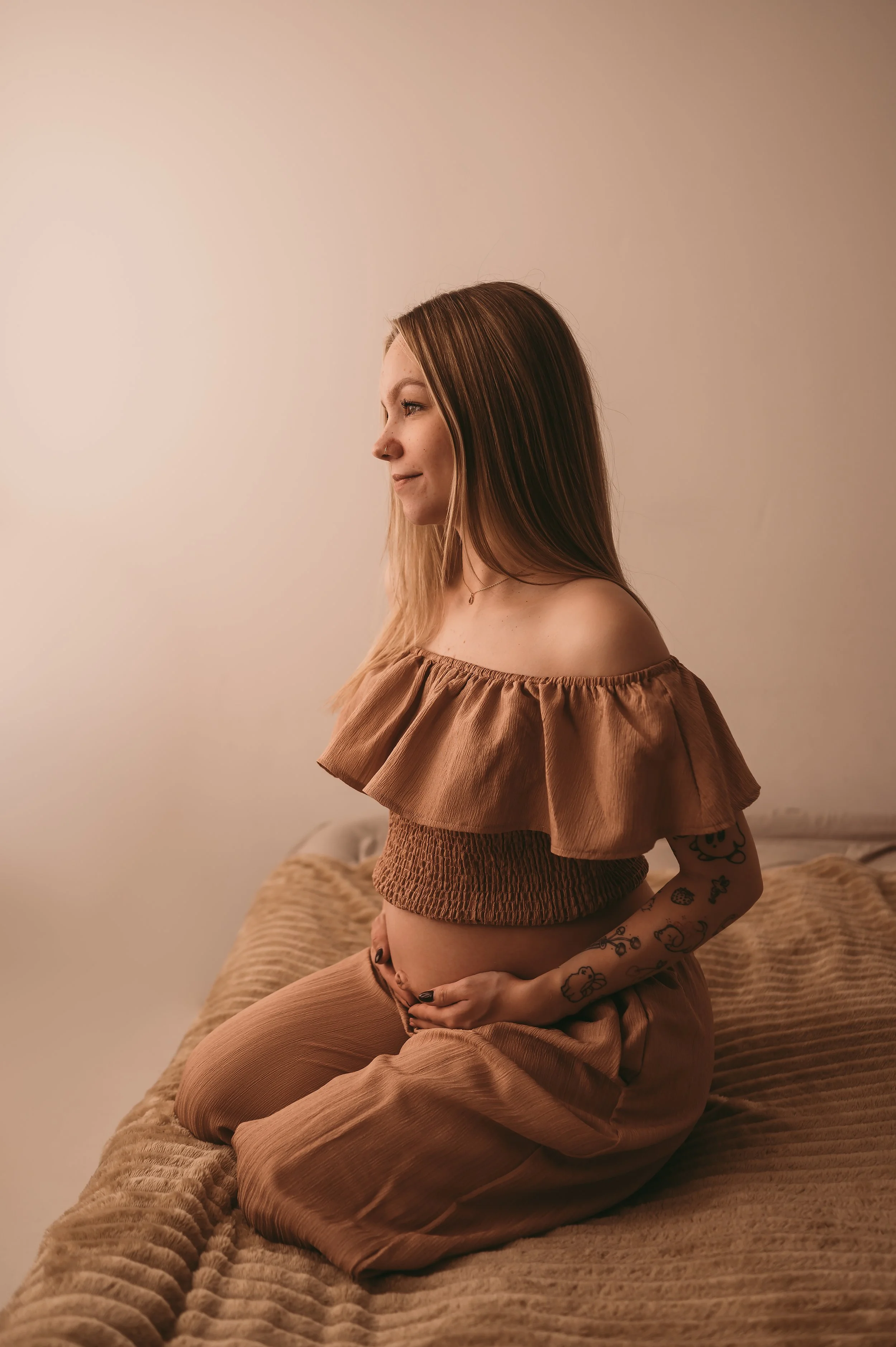 Mother to be sat on a bed, facing a window, holding baby bump,  Maternity photography by kp-photo, based in Wiltshire