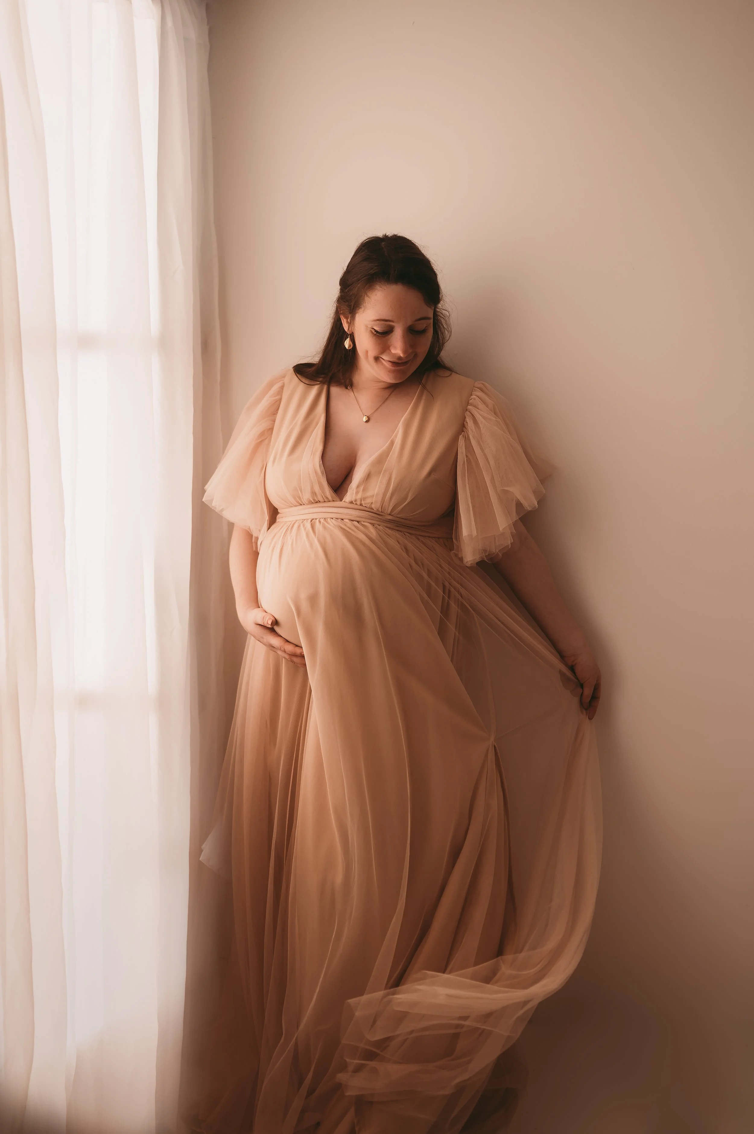 Woman wearing a Maternity dress, big and made of tulle, swishing the fabric whilst holding baby bump being photographed by KP-Photo, Wiltshire