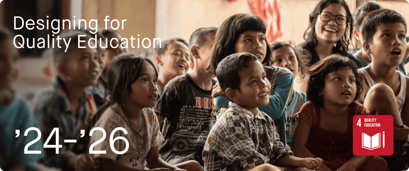 Group of children and a woman smiling and watching a presentation or performance in a classroom environment, with a focus on engagement and education.