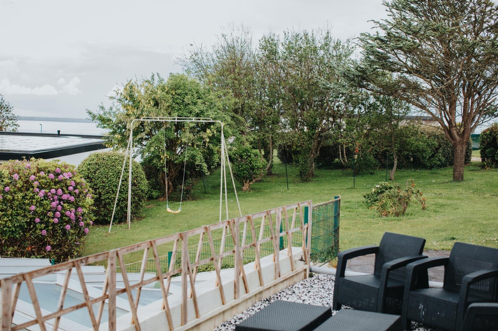 Jardin avec balançoire, buissons fleuris, arbres et mobilier d'extérieur.