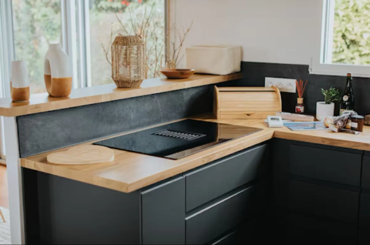 Cuisine avec comptoir en bois clair, plan de cuisson électrique noir, décorations en céramique et plantes.