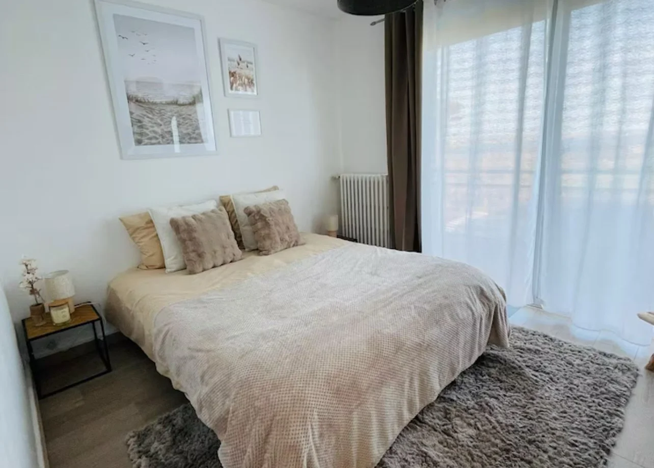 Chambre avec lit, coussins, tapis à poils longs, rideaux et tableaux muraux.