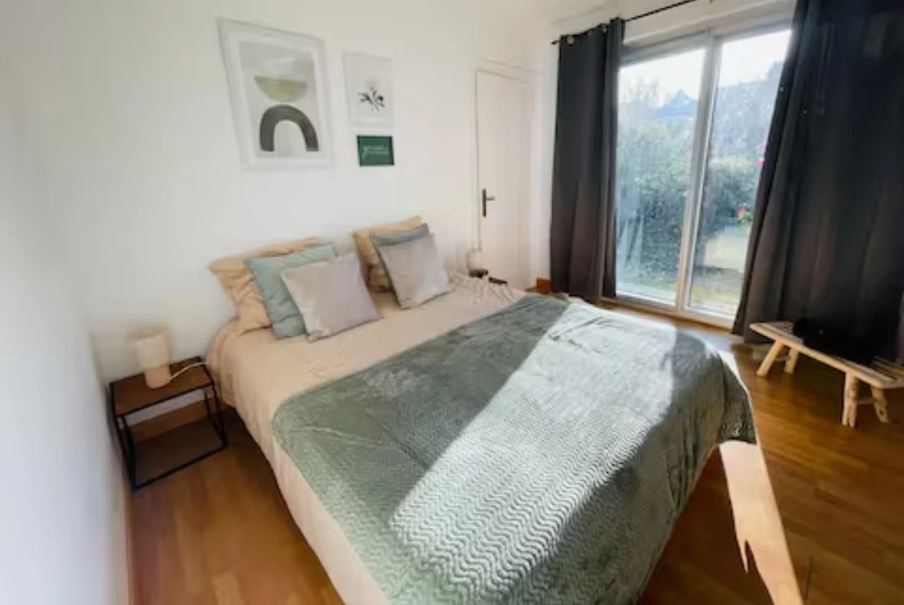 Chambre avec lit double, oreillers, table de nuit avec lampe, grande fenêtre avec rideaux noirs, murs blancs, décoration murale minimaliste.